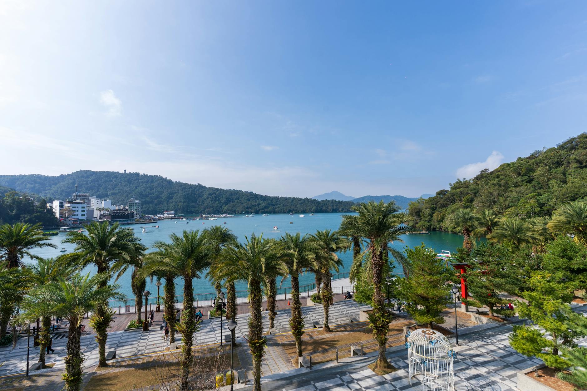 Beautiful view of Sun Moon Lake with palm-lined walkways, blue skies, and serene waters.