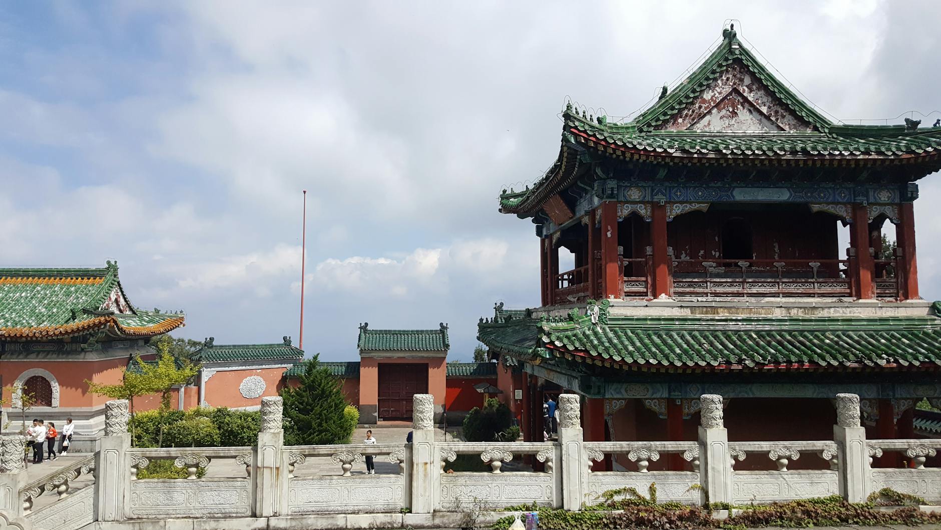Beautiful traditional Chinese buildings with intricate green roofs set against a cloudy sky.
