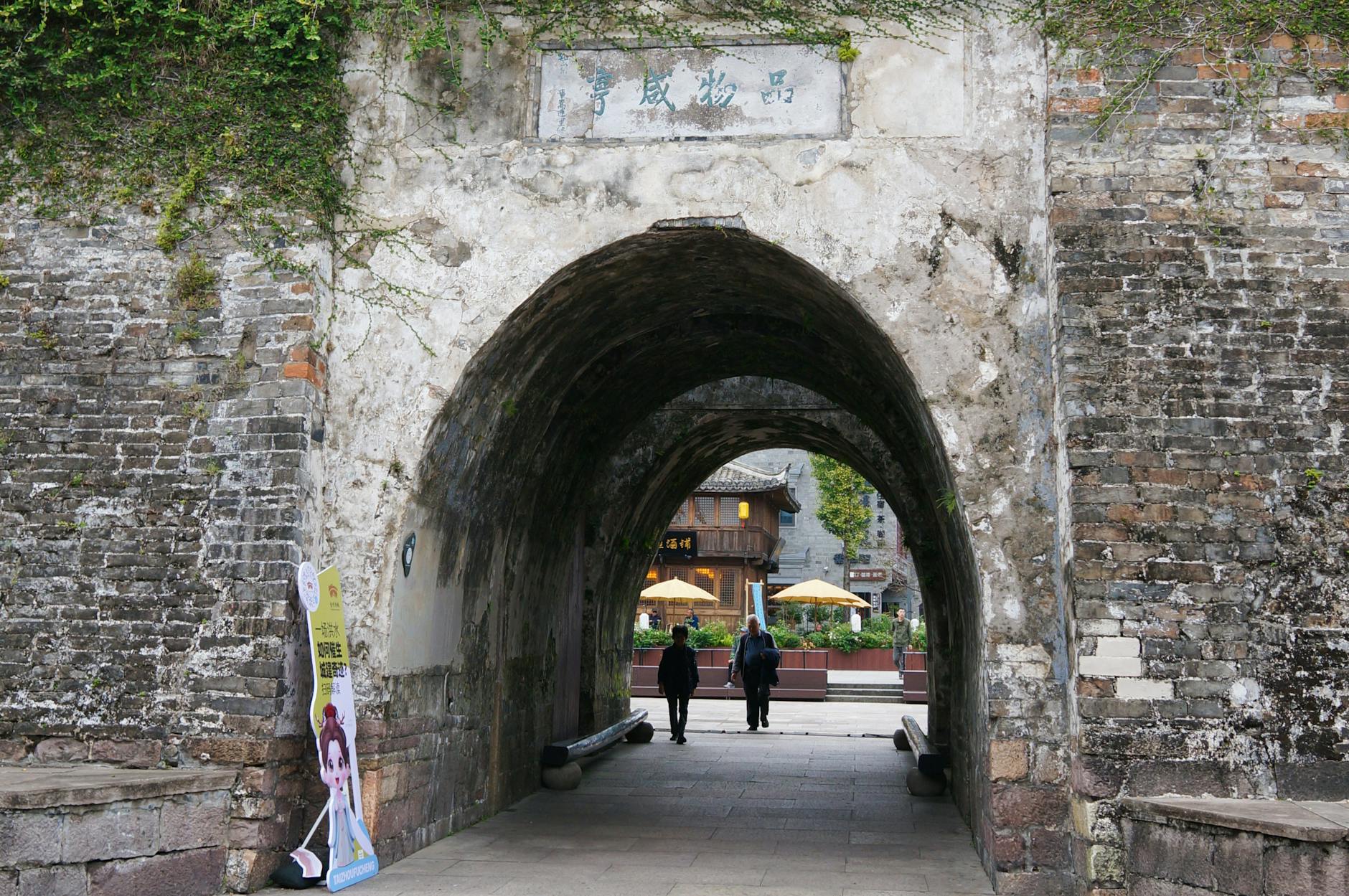 Ancient stone gate entrance leading to a historic city center with visible signage.