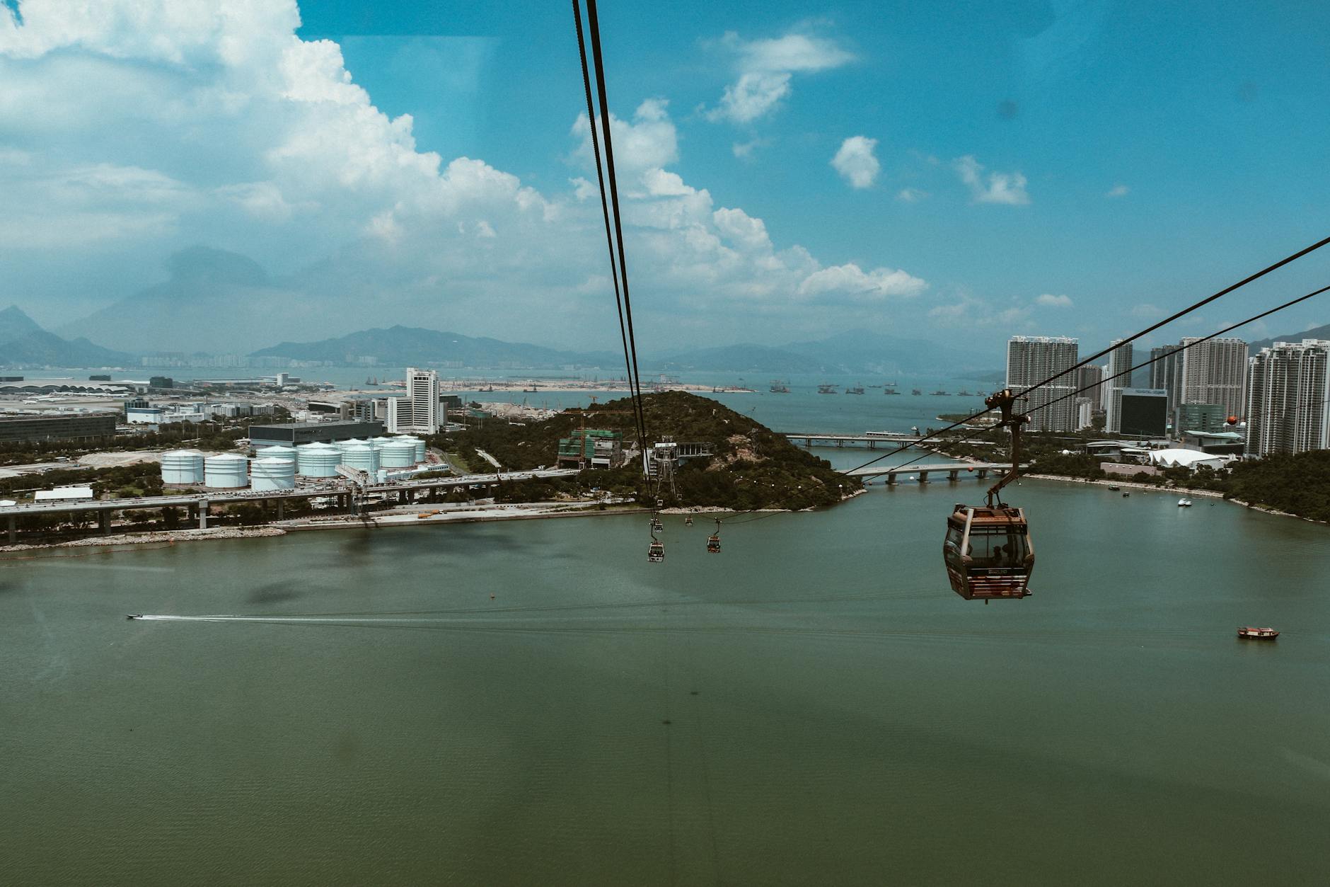Experience breathtaking views from a cable car over a bustling harbor cityscape with sprawling mountains in the backdrop.