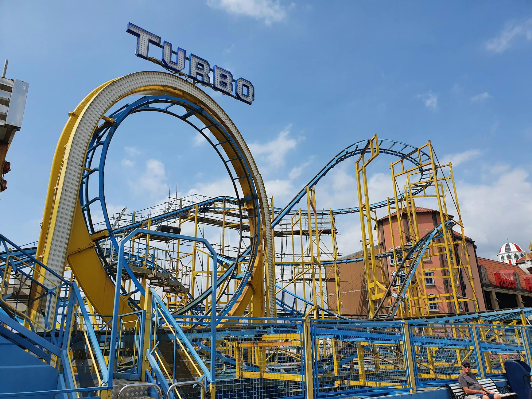Dynamic view of a colorful roller coaster against a clear blue sky.