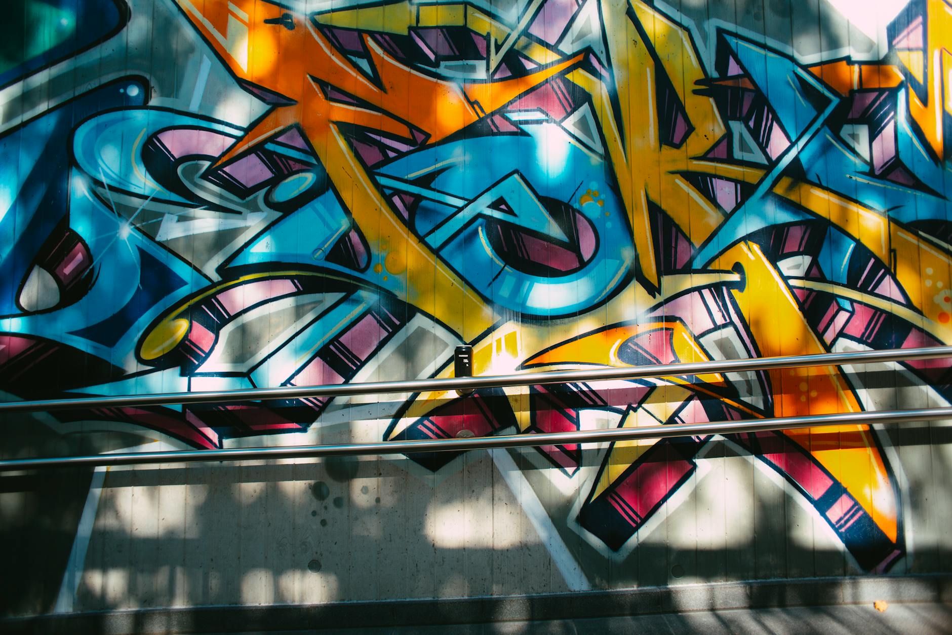 Colorful graffiti art on a city wall with metal railings in sunlight, showcasing urban creativity.
