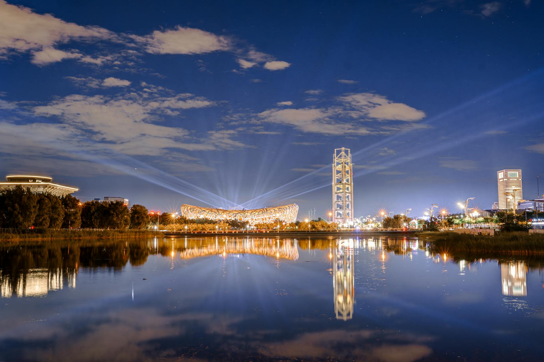Illuminated nightscape of Beijing's Bird Nest Stadium reflecting on a serene lake.