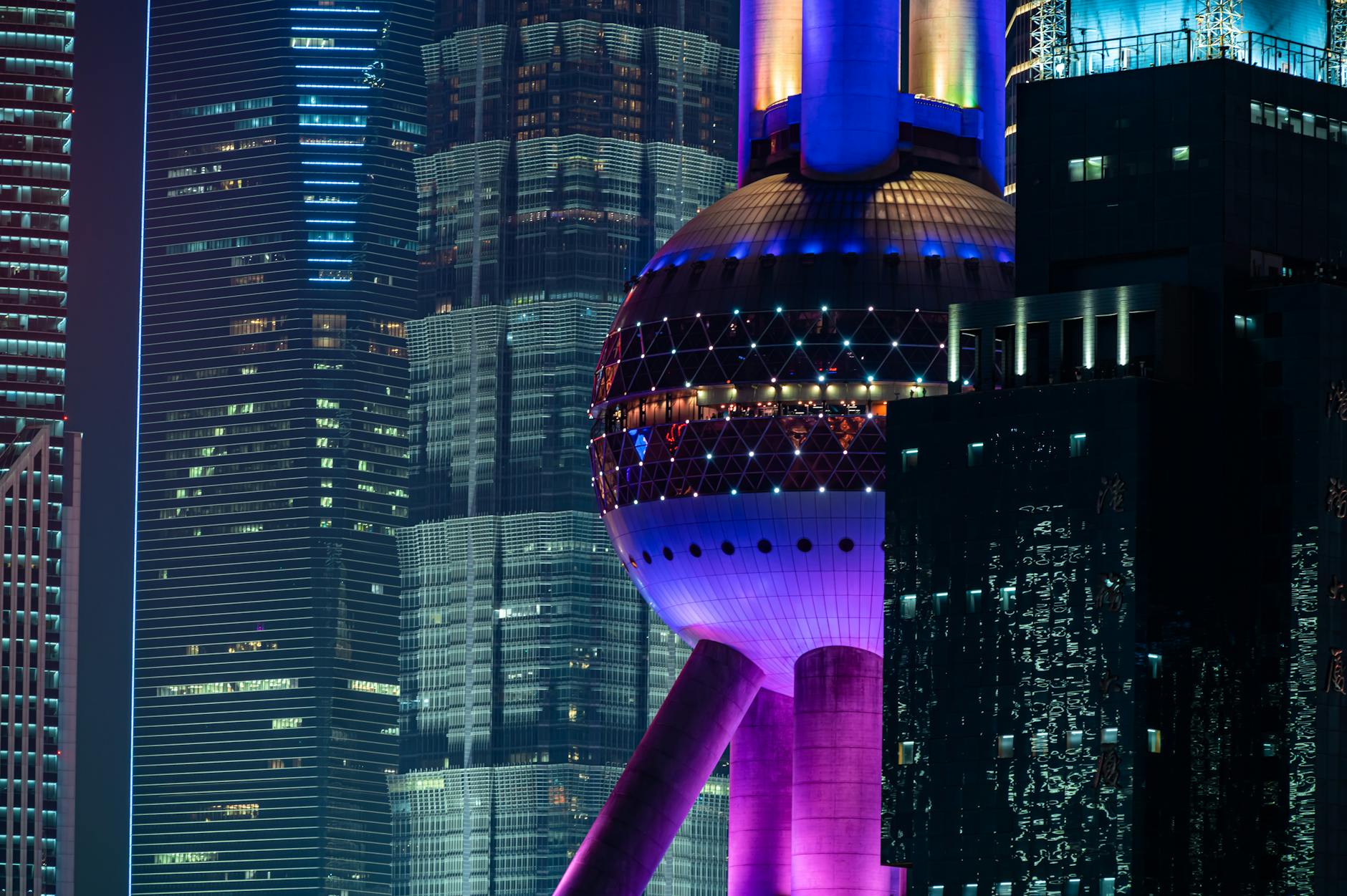 Vibrant night scene featuring the iconic Oriental Pearl Tower in Shanghai with illuminated skyscrapers.