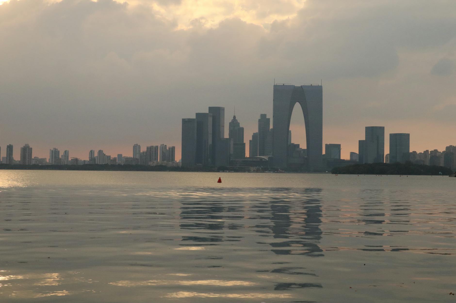Serene sunset view of Suzhou skyline reflected over Jinji Lake with moody clouds.