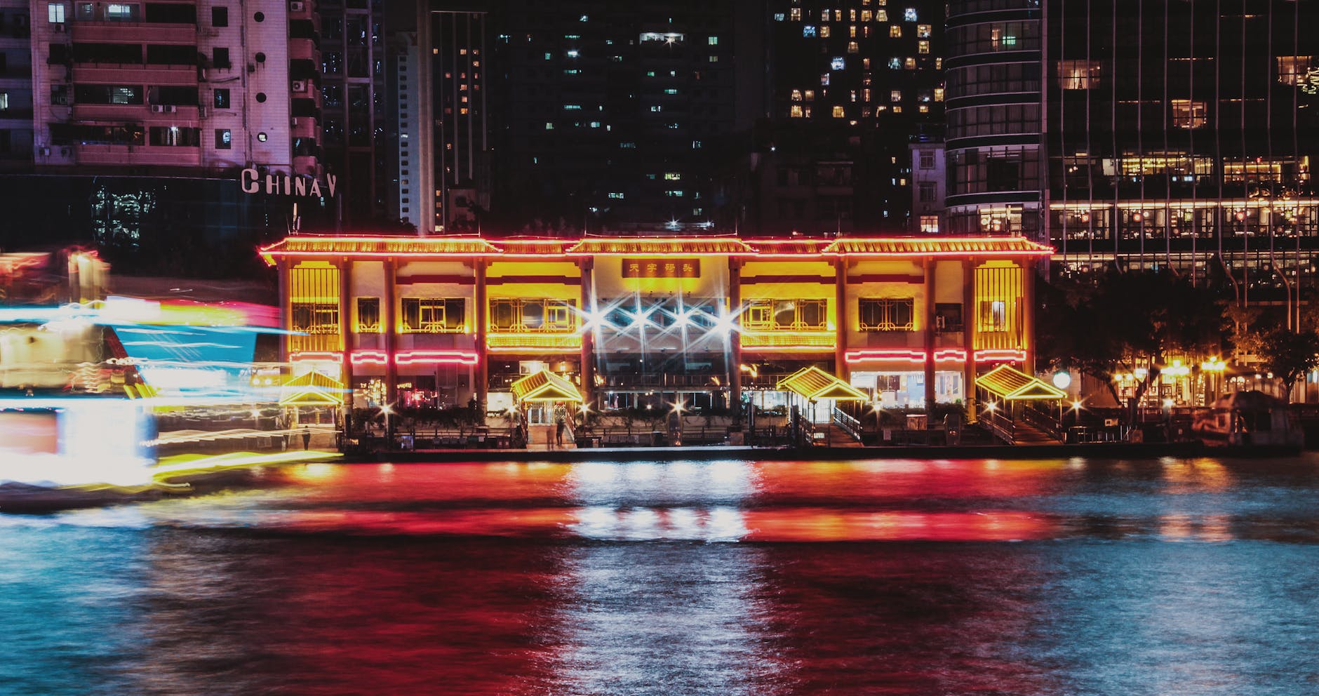 Illuminated riverside building in Guangzhou with colorful reflections at night.
