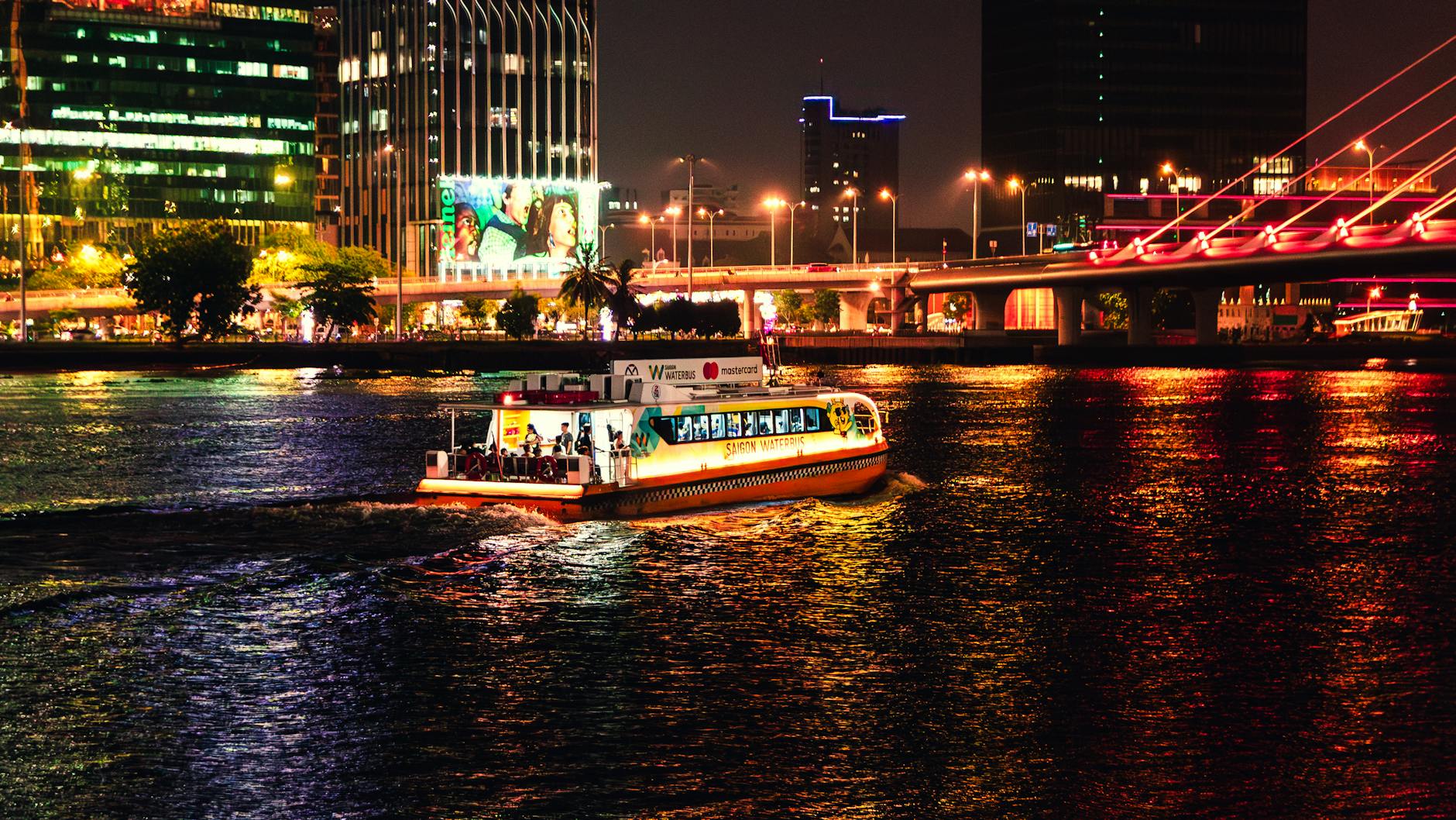 Illuminated boat cruises the Saigon River at night, showcasing Ho Chi Minh City's lively skyline.