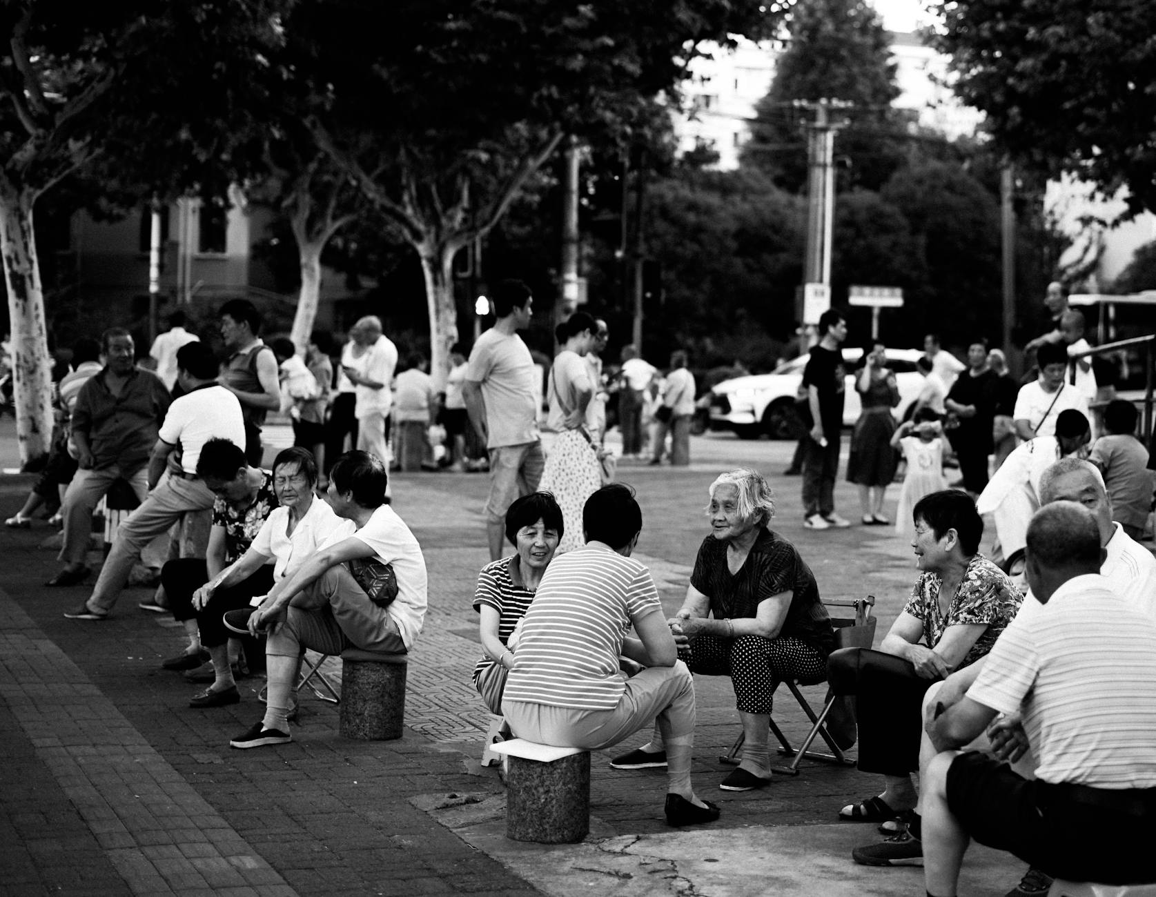 Black and white image of people socializing in a lively Shanghai town square.