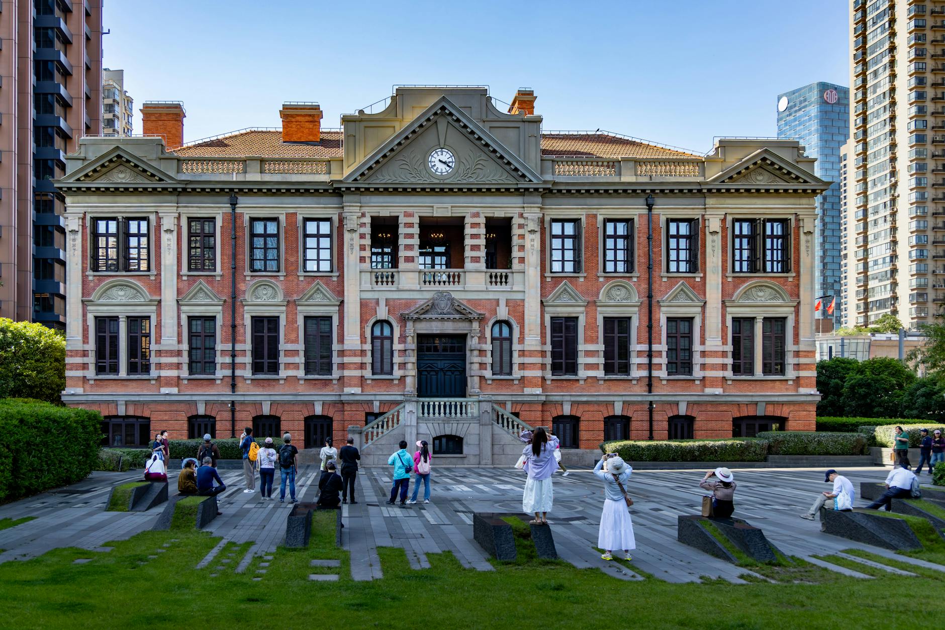A historic building with visitors in front, set against a modern urban skyline during the day.