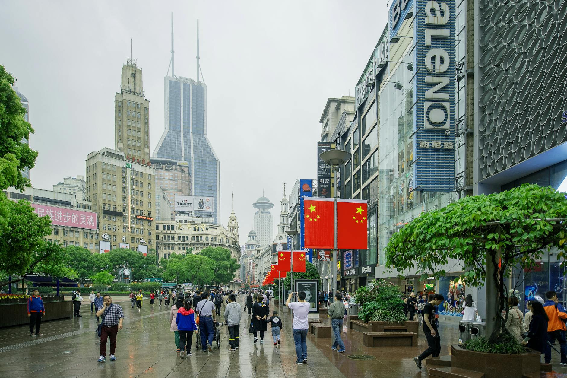 Pedestrians walking on Nanjing Road, Shanghai amidst skyscrapers on a cloudy day.