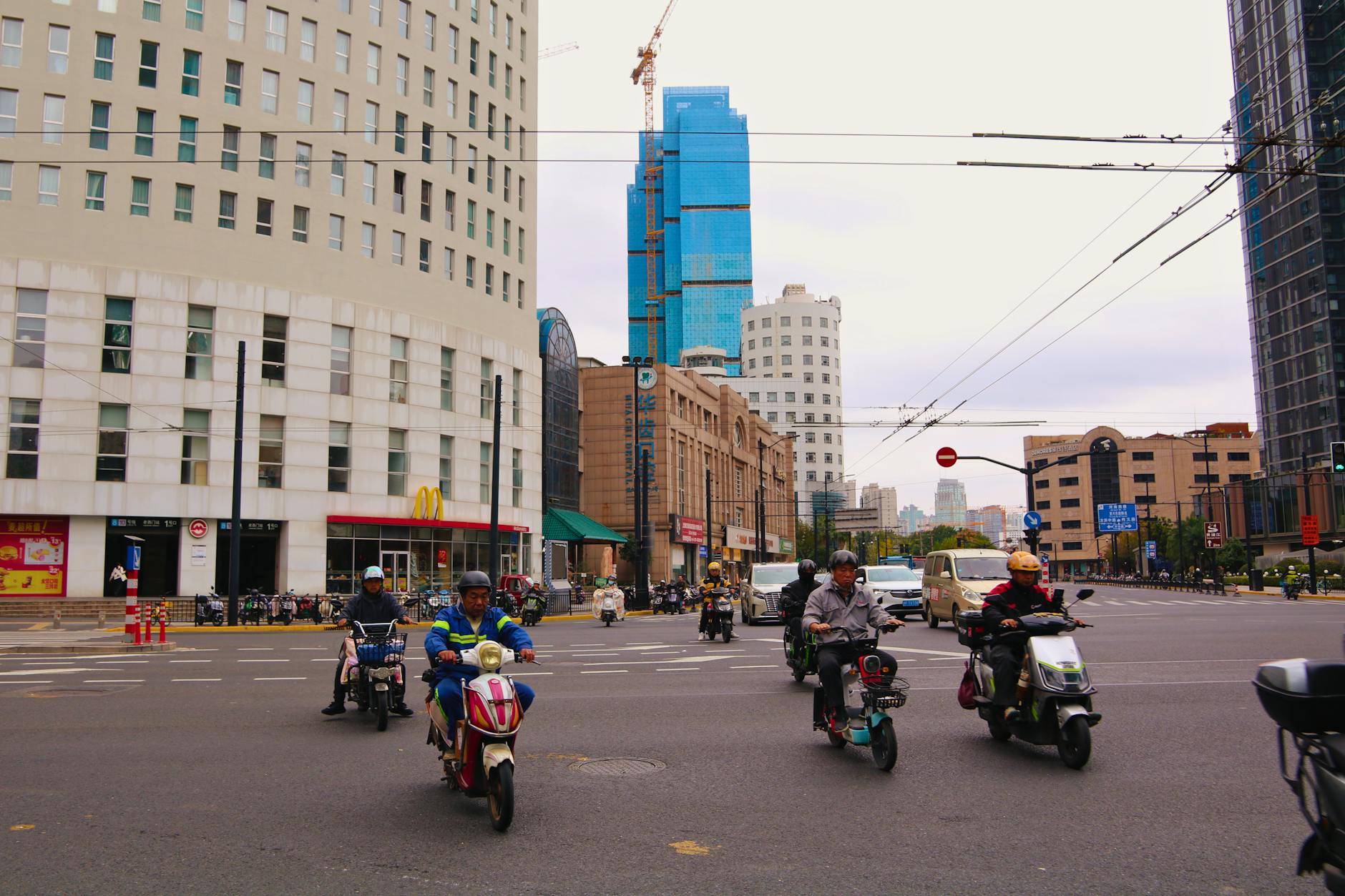 Motorcyclists navigating a bustling intersection in Shanghai, China, surrounded by modern skyscrapers.