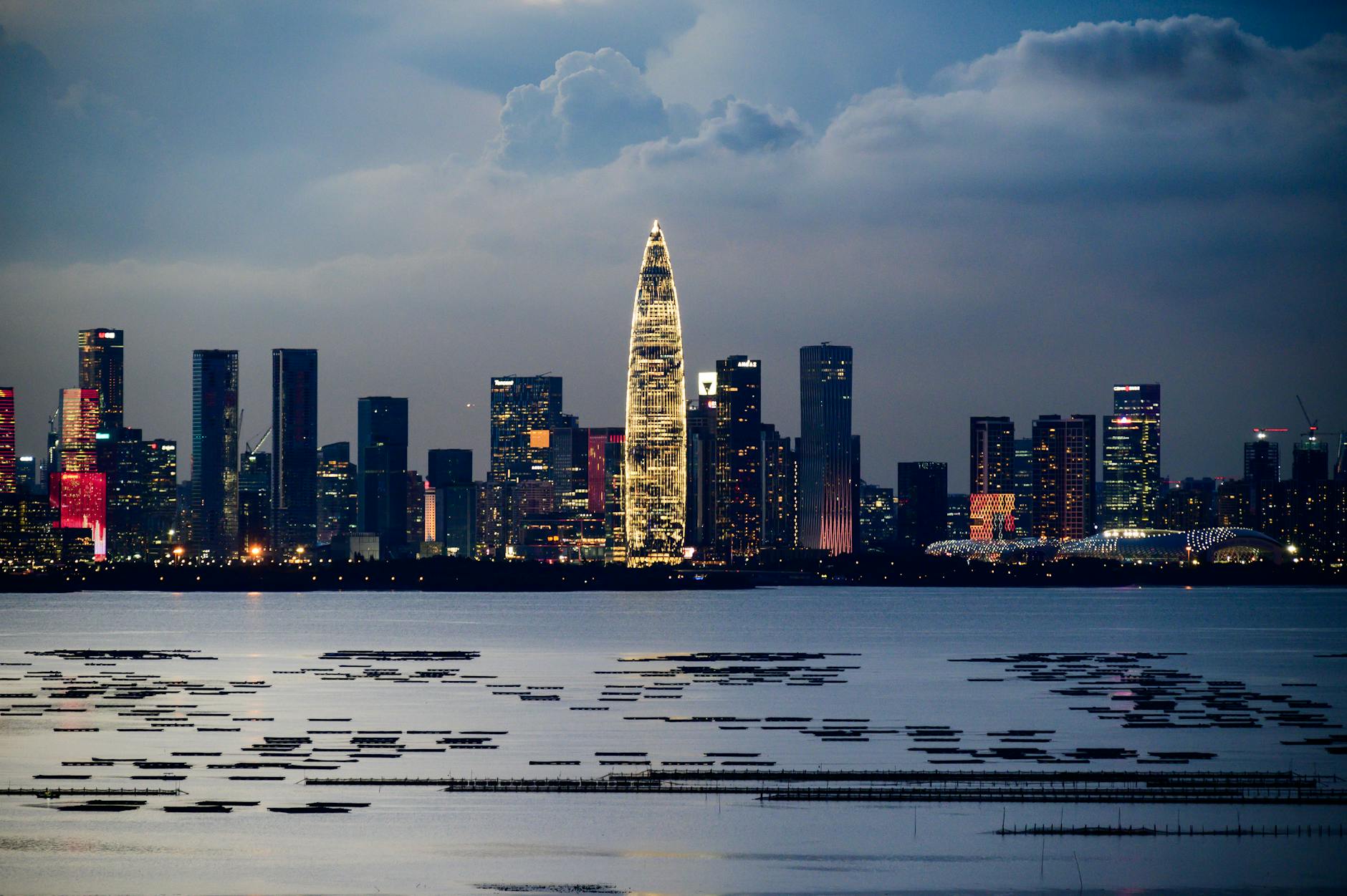 Stunning urban skyline reflecting on waterfront during twilight, showcasing city lights and modern architecture.