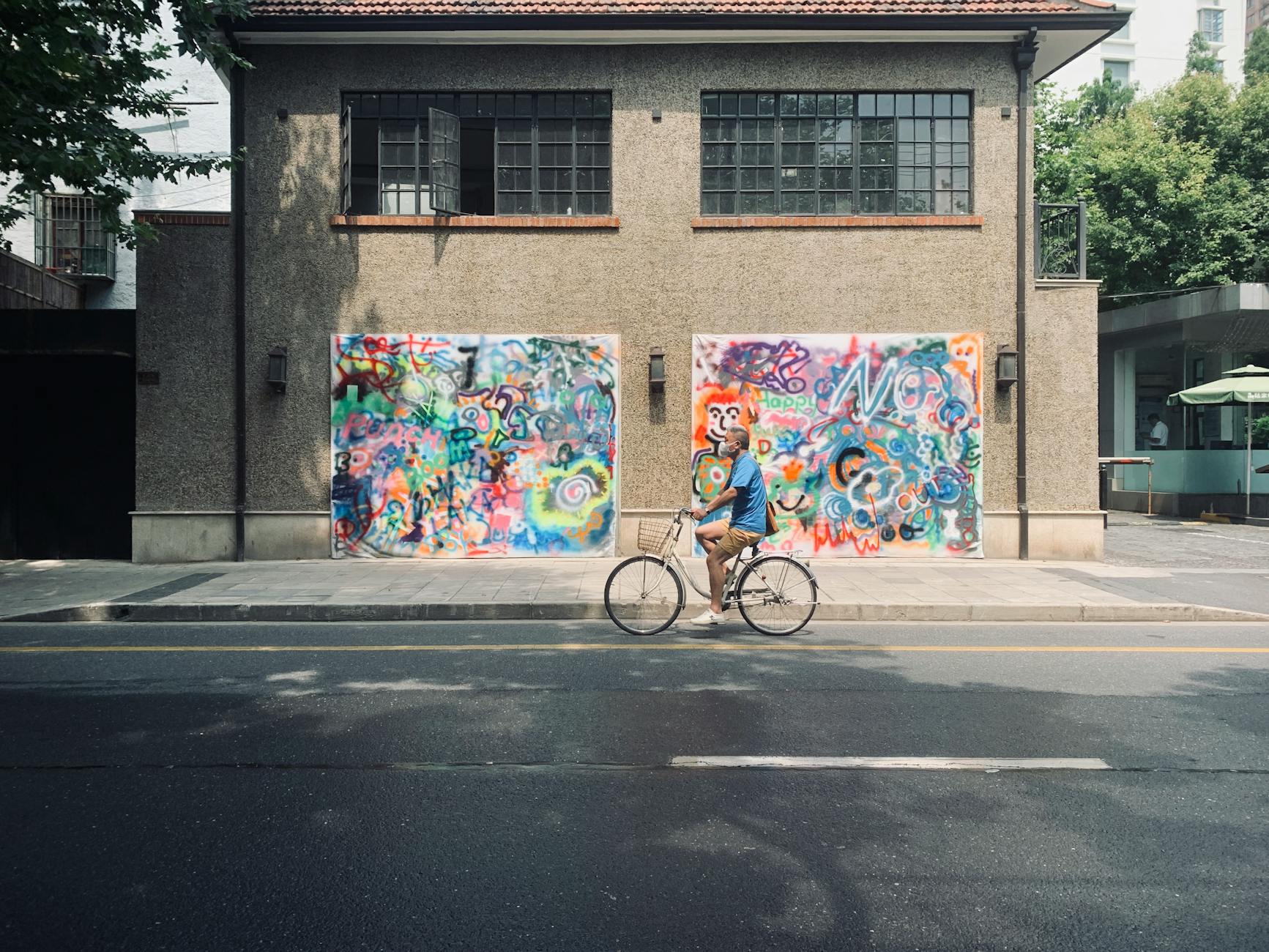 A cyclist rides past vibrant graffiti on a sunny street in Shanghai, China.