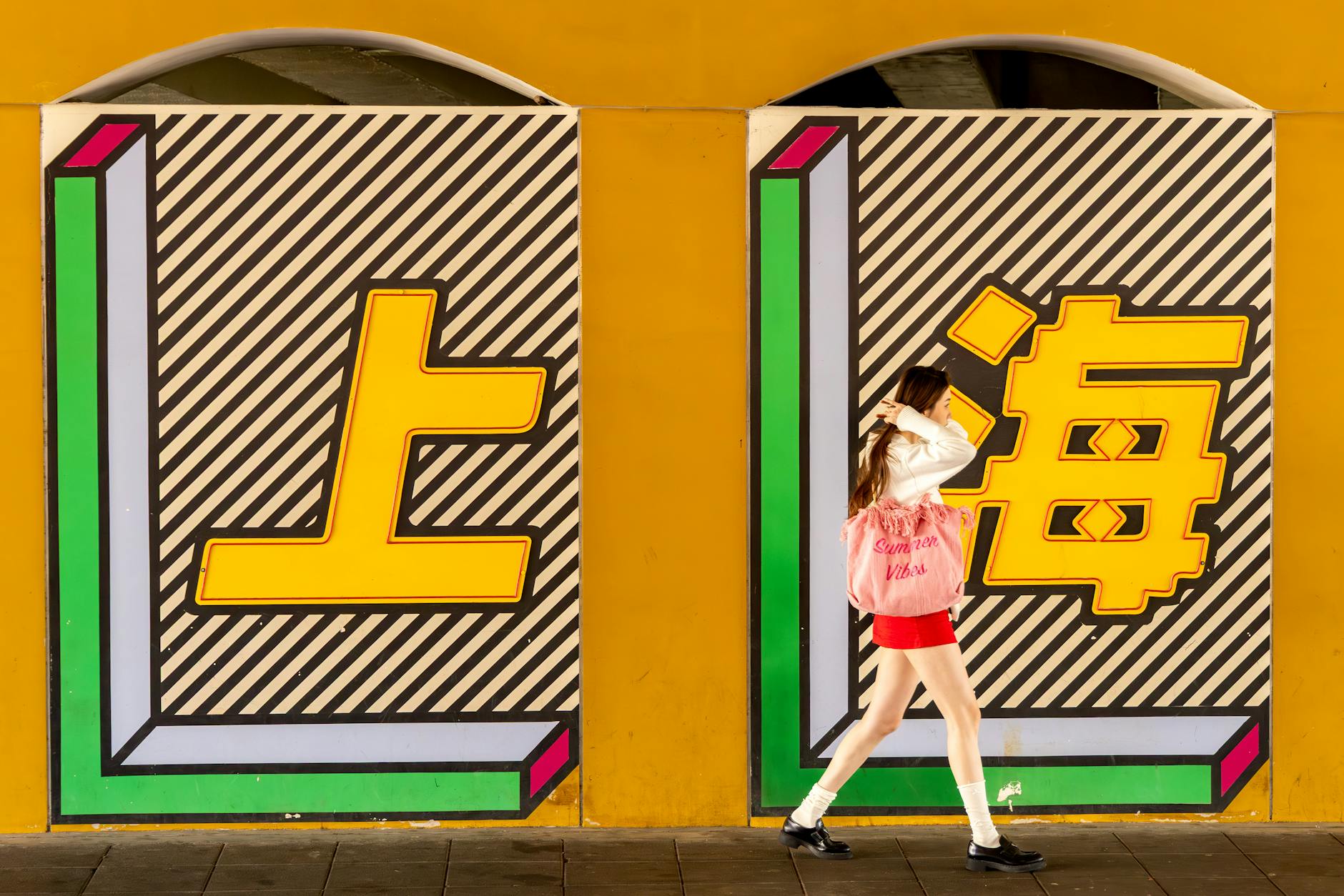 A woman walks past a colorful mural depicting Shanghai. Bright and artistic street scene.