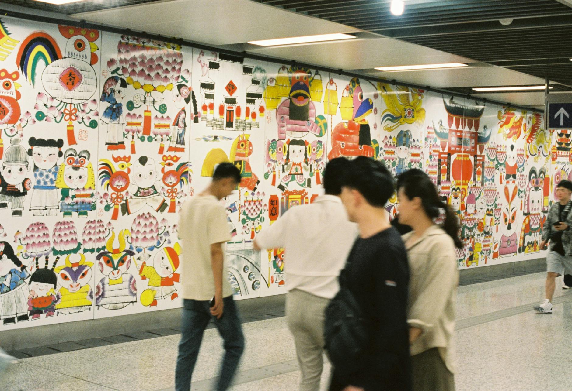 Blurry pedestrians pass a vibrant cultural wall in Nanjing Metro, capturing urban life.