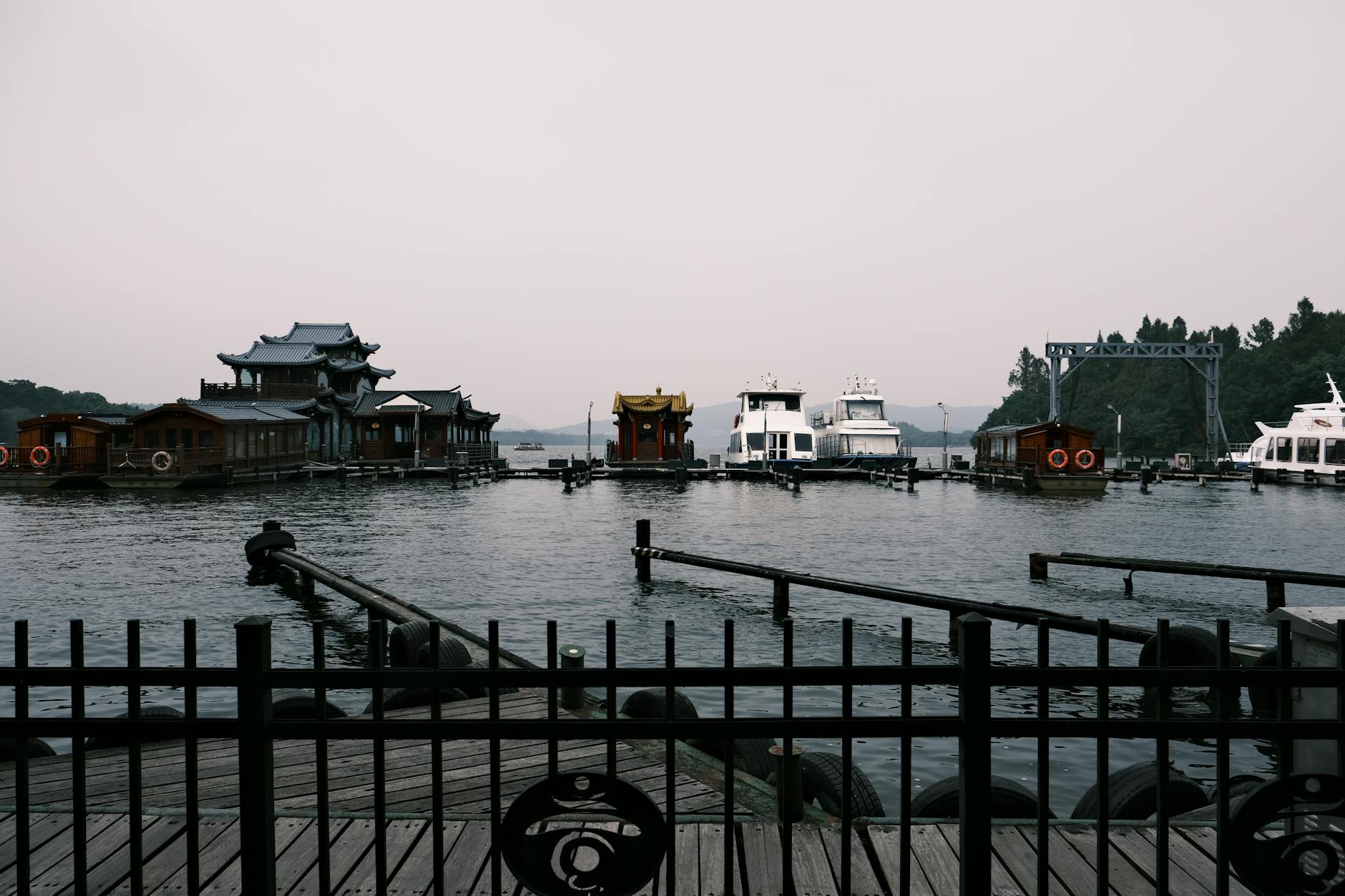 Serene view of historic boats and structures on West Lake in Hangzhou, China, with misty mountains.