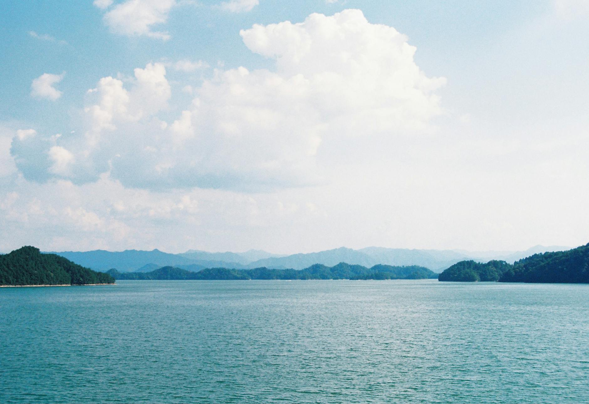 Serene lake view with distant mountains and a bright, cloudy sky.