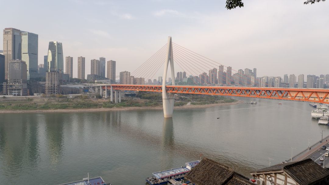 Orange bridge spans river with city skyline behind.