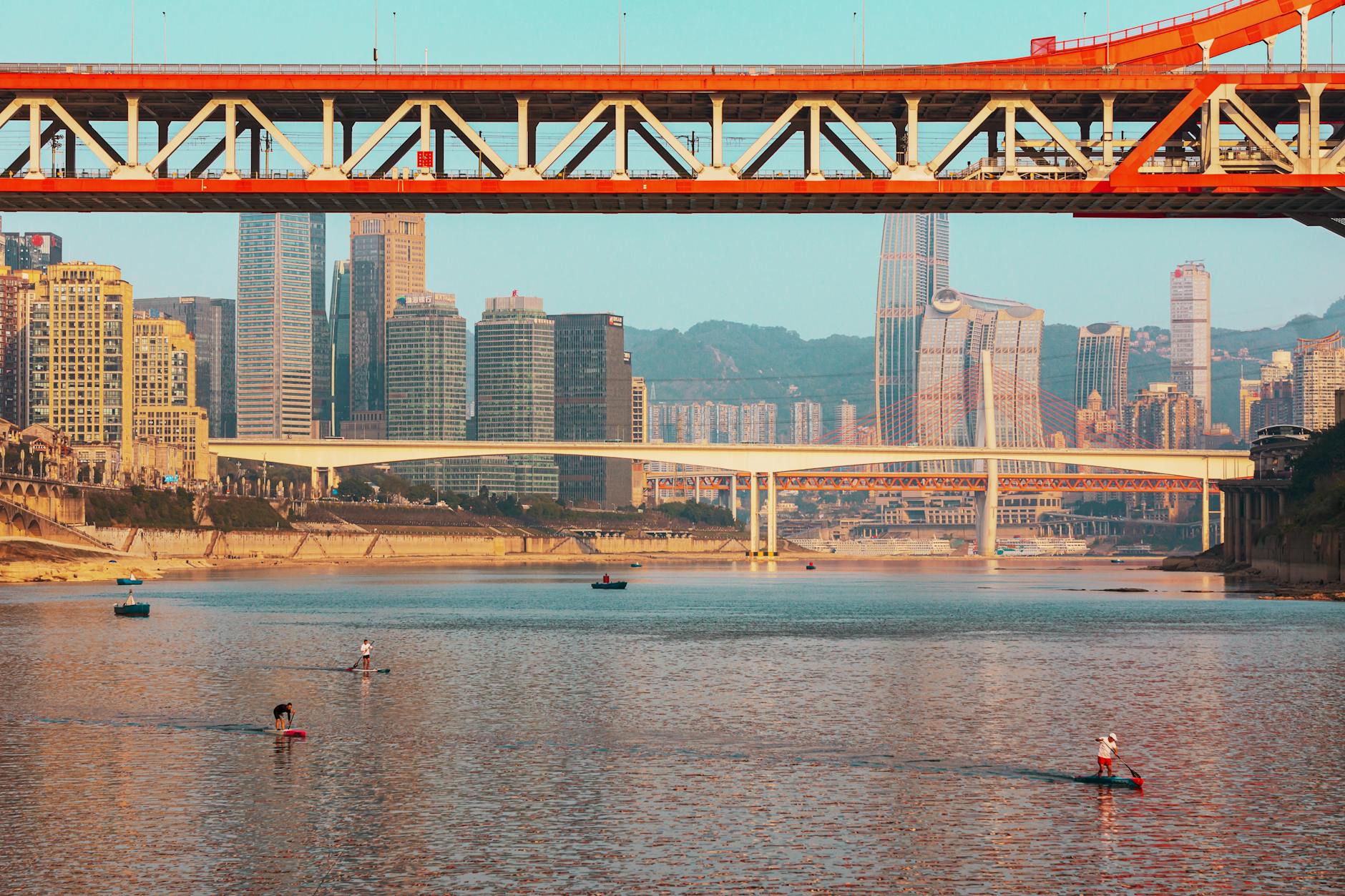 Scenic view of a bustling city with bridges and paddleboarders on the river.