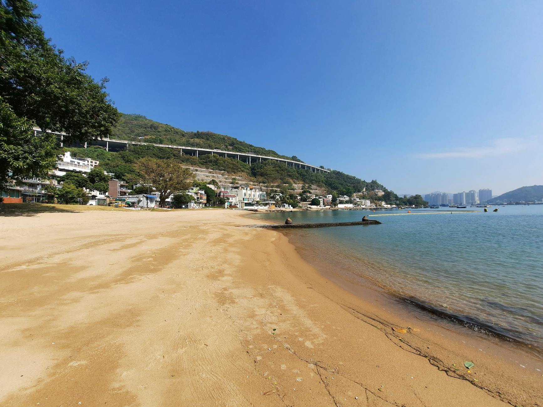 A serene beach with golden sand, clear water, and a city skyline in the background.