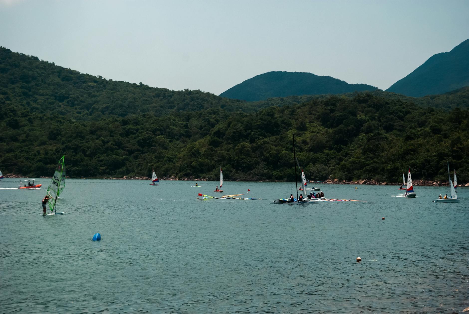Enjoy windsurfing and sailing in Hong Kong's picturesque waters, framed by lush green hills.