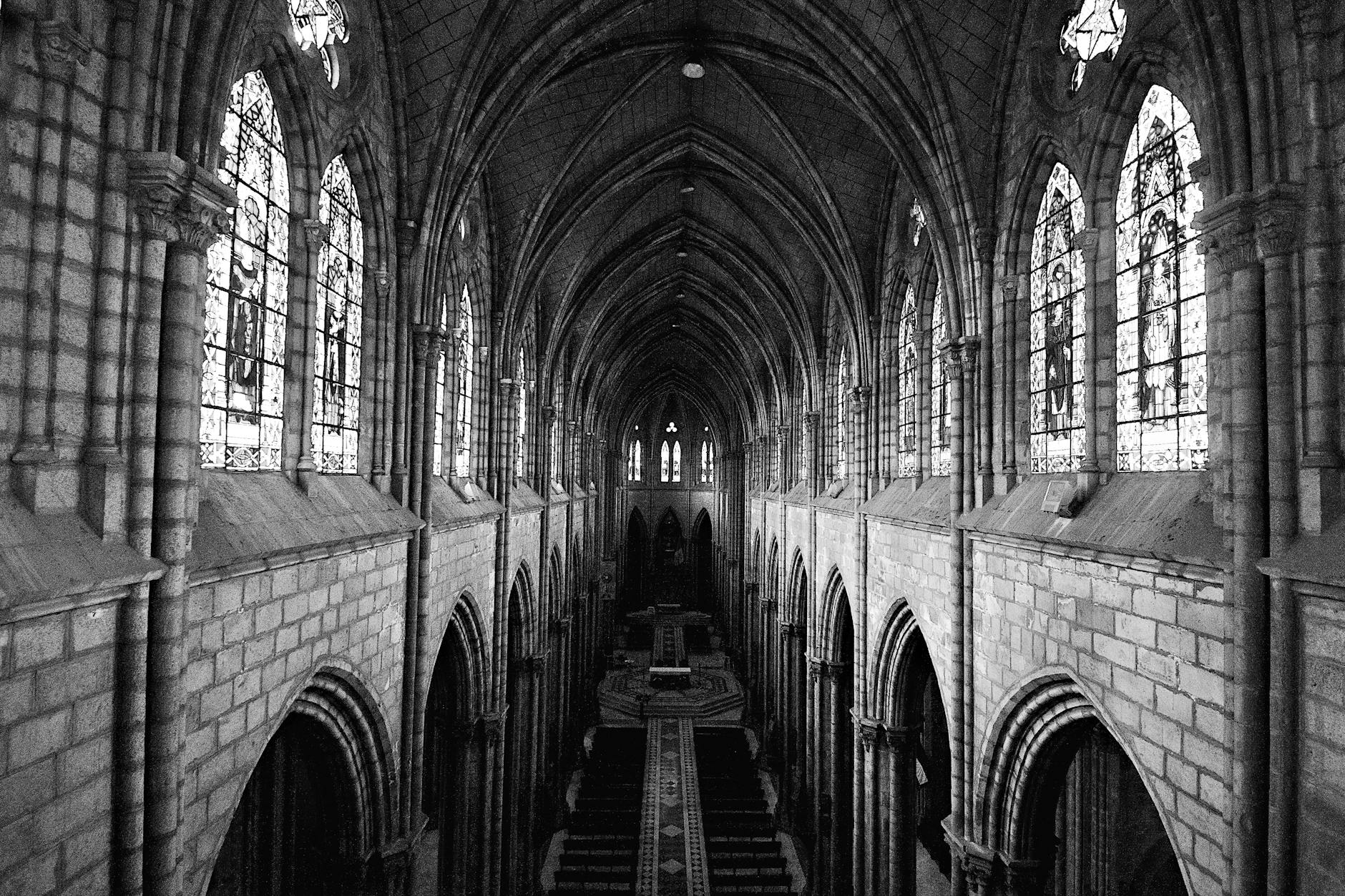 Black and white photo showcasing the majestic interior of a gothic cathedral with stained glass windows.