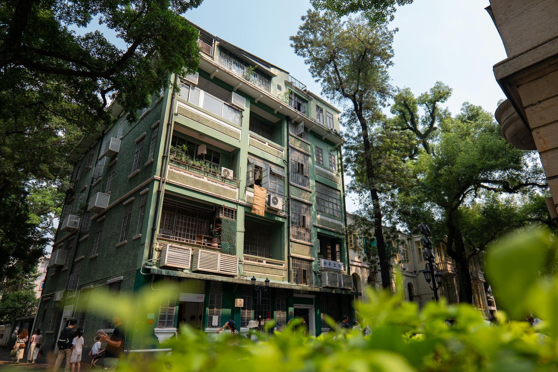 Vintage green building surrounded by lush trees and urban street life, showcasing historical architecture.