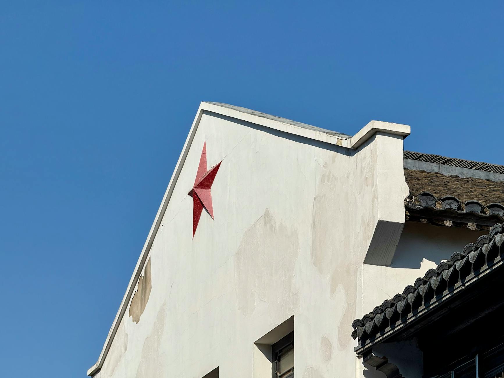 A red star on a white traditional Chinese building facade under clear blue skies.