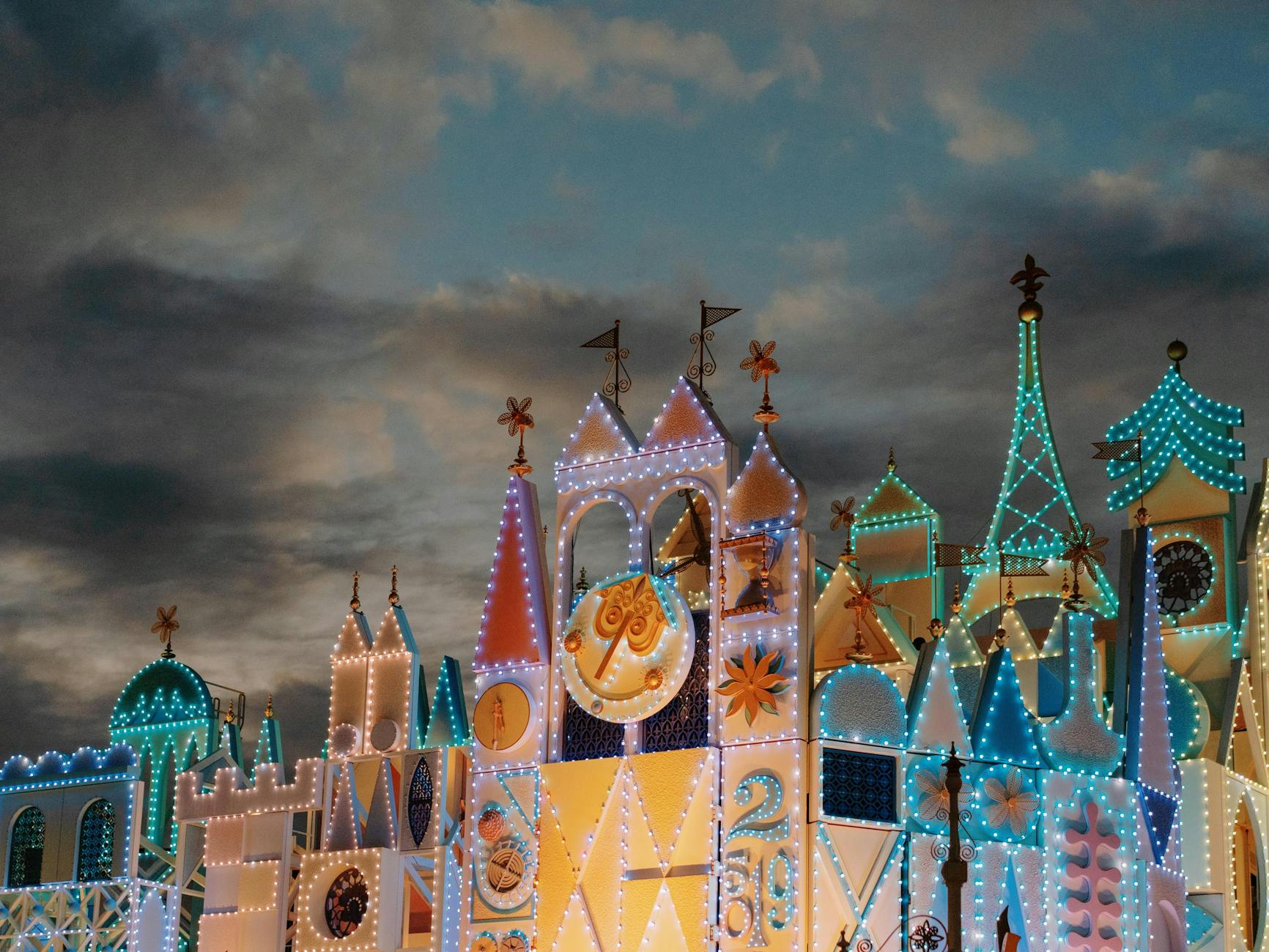 An enchanting view of a fairy tale castle adorned with colorful lights against a dramatic evening sky.