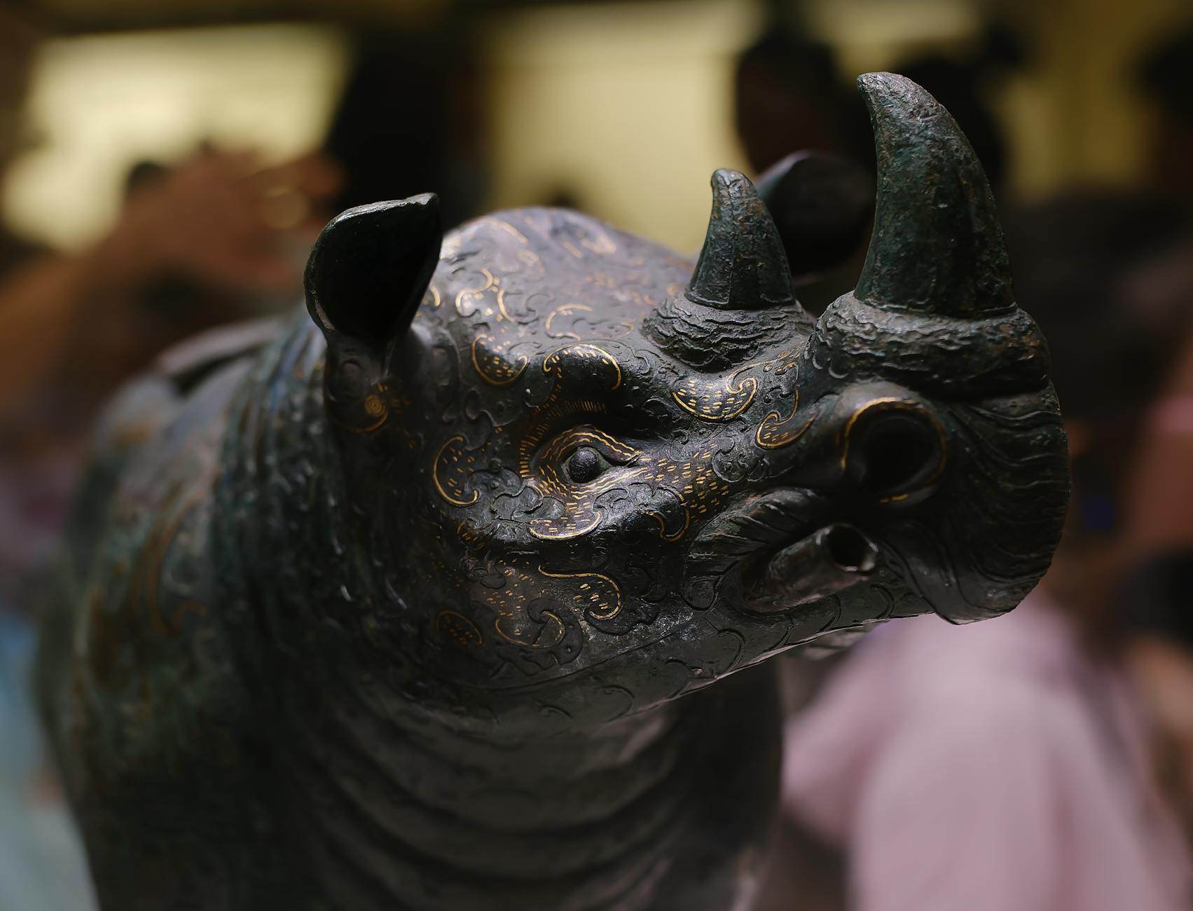 Detailed close-up of a bronze rhinoceros sculpture with ornate patterns exhibited indoors.
