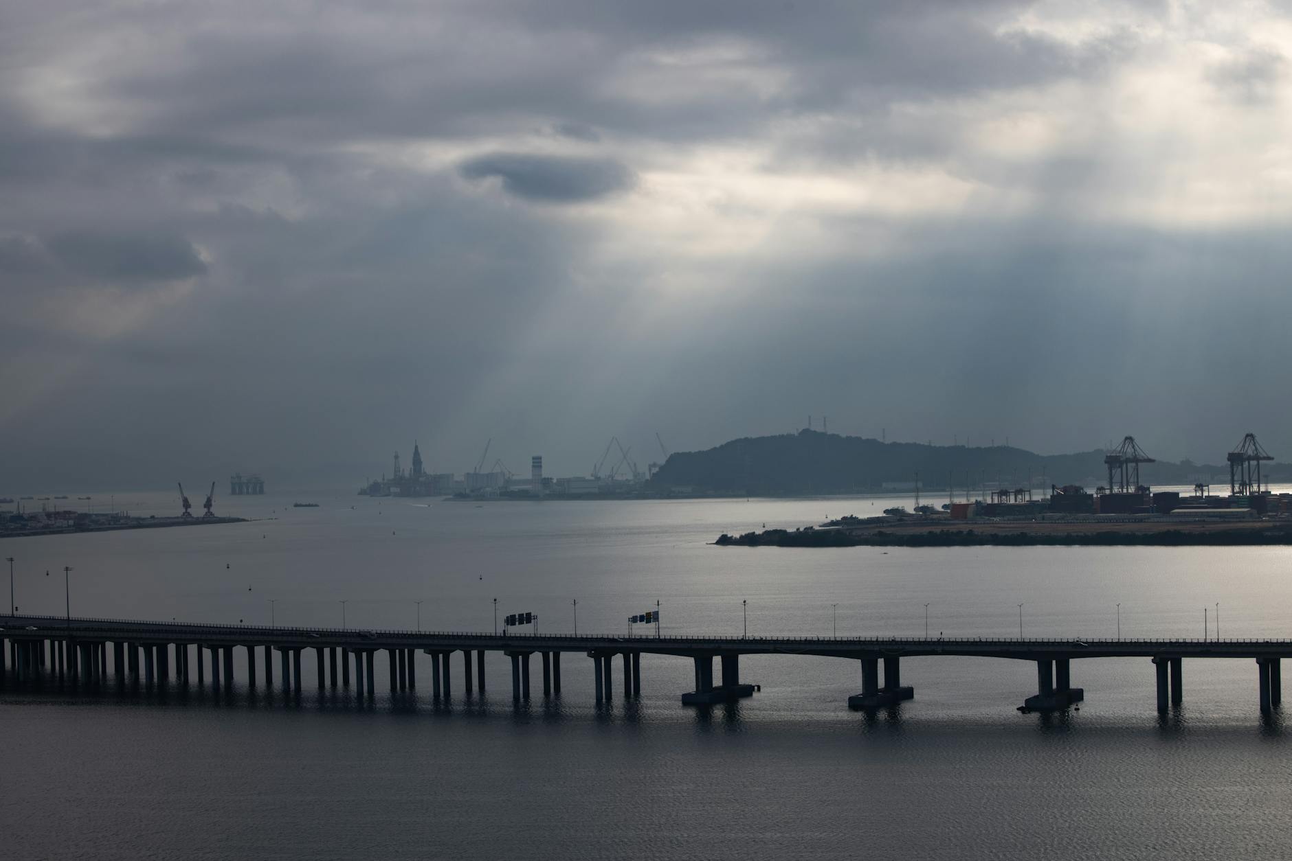 Aerial view of Shenzhen port and bridge under a dramatic cloudy sky with sunbeams breaking through.