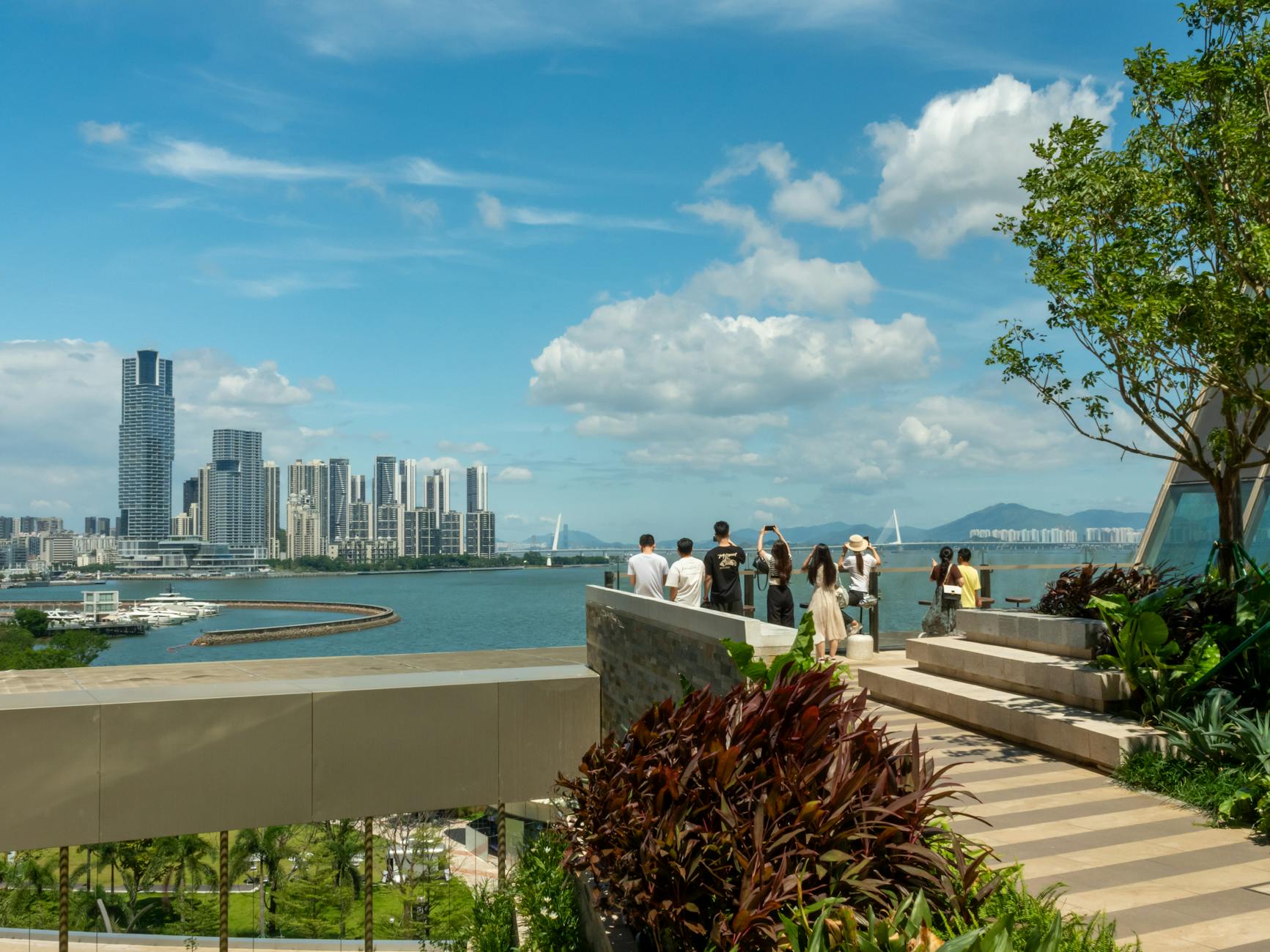 Scenic view of Shenzhen Bay with people enjoying the skyline from a green terrace.