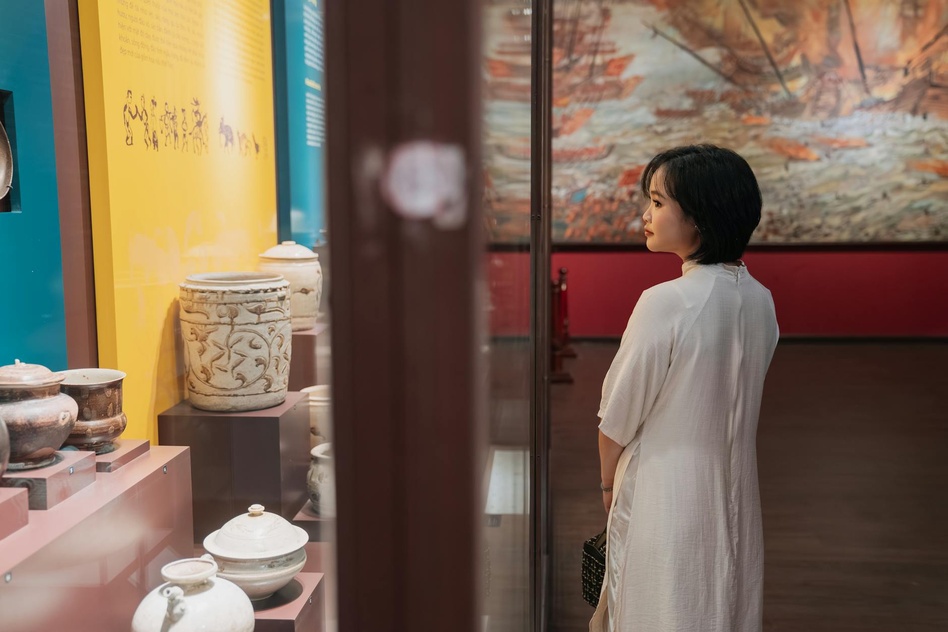A woman engaging with historical artifacts in a museum exhibit setting, reflecting on culture.