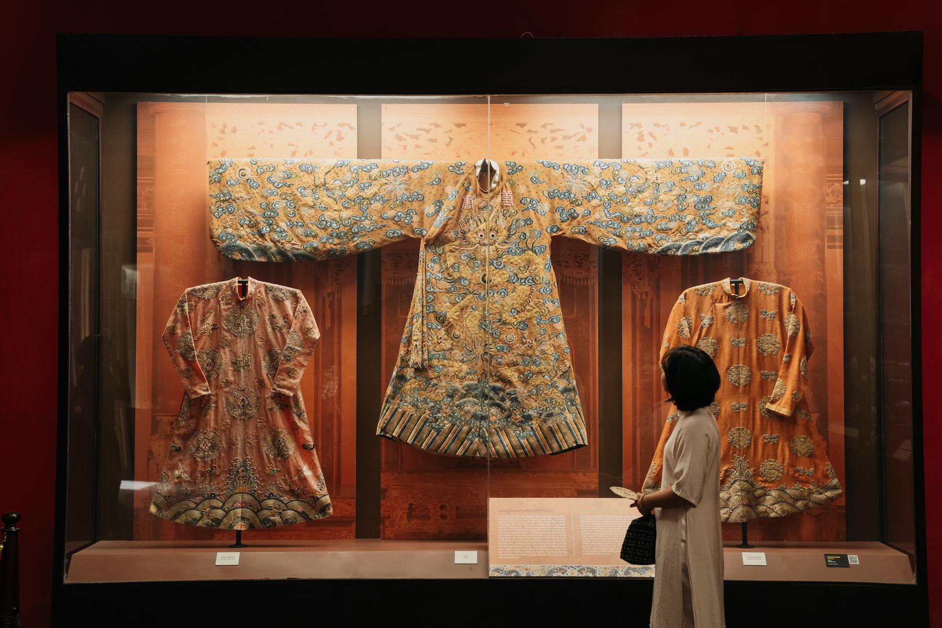 Exquisite traditional Chinese robes displayed in a museum with a visitor observing.