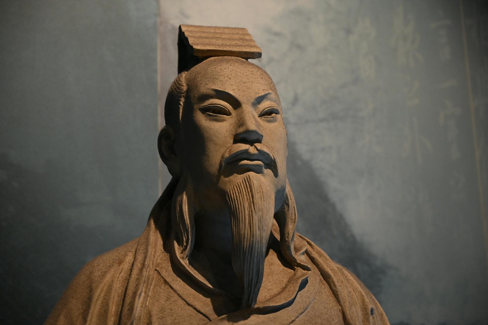 A detailed ancient statue of an Asian figure with traditional attire and expressive features.
