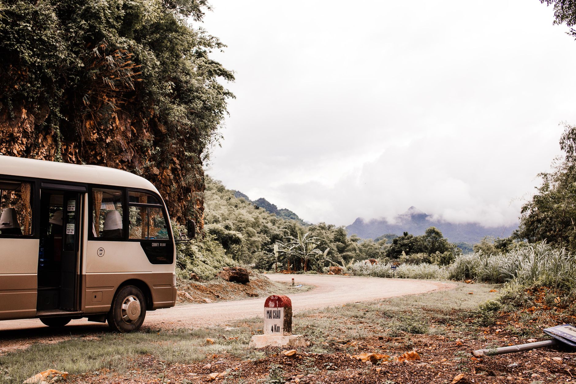 Shuttle bus on a winding road with mountainous backdrop and lush greenery.