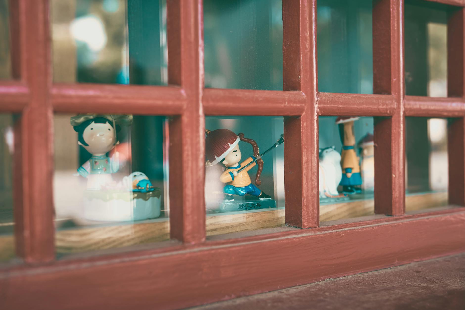Cute figurines displayed on a windowsill, framed by traditional Chinese architecture.