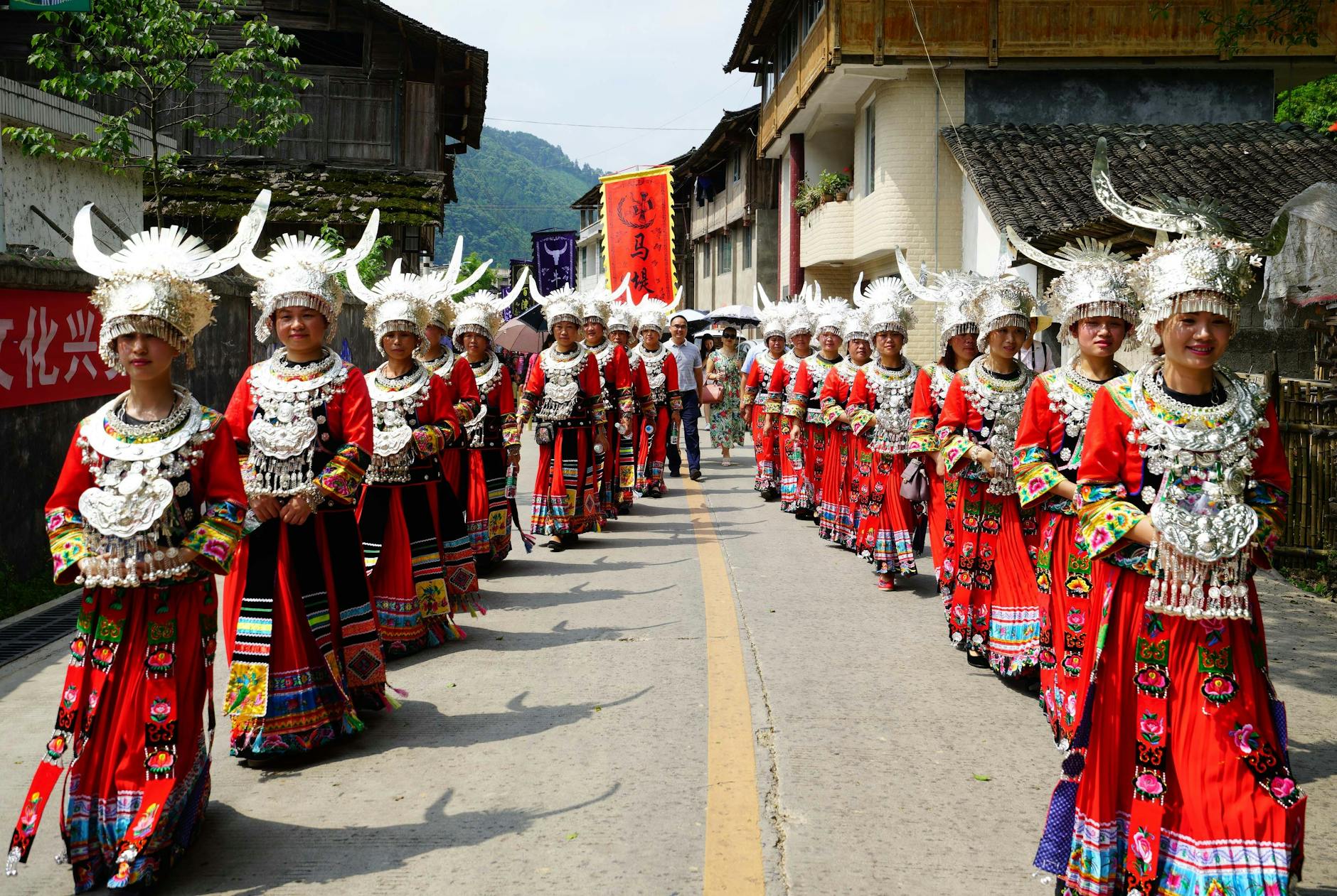Colorful Miao women in traditional attire during a street parade in rural China.