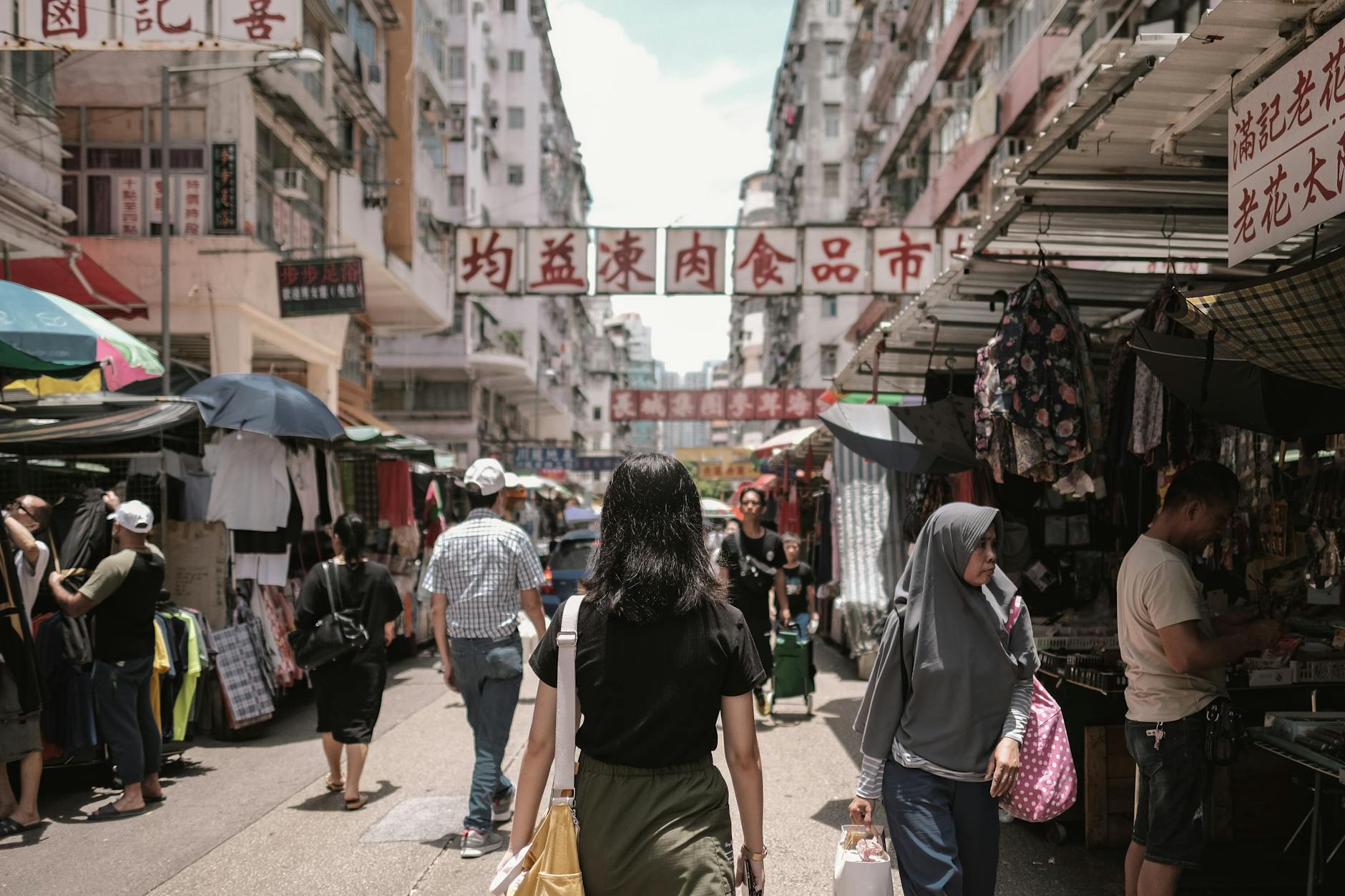 Bustling Hong Kong market street with diverse people and colorful stalls under bright signs.