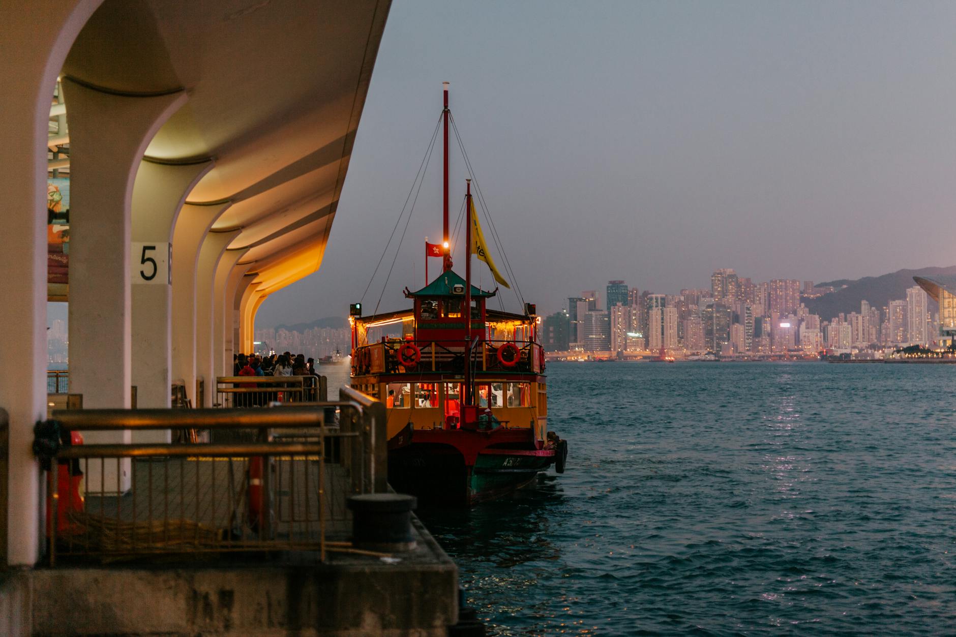 Vibrant ferry moored at Hong Kong harbor with city skyline and colorful twilight.
