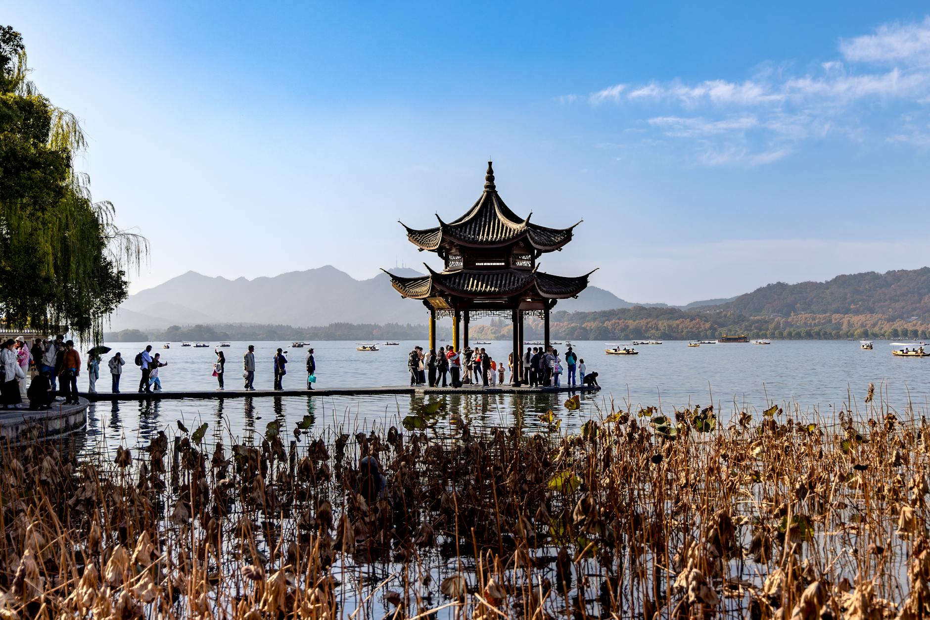 Visitors admire a traditional pagoda on West Lake, surrounded by serene water and mountains in Hangzhou.