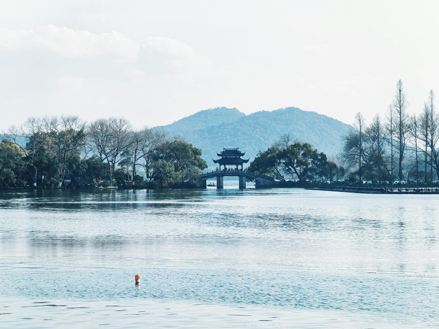 Tranquil view of West Lake featuring a traditional pavilion amidst serene waters and distant hills.