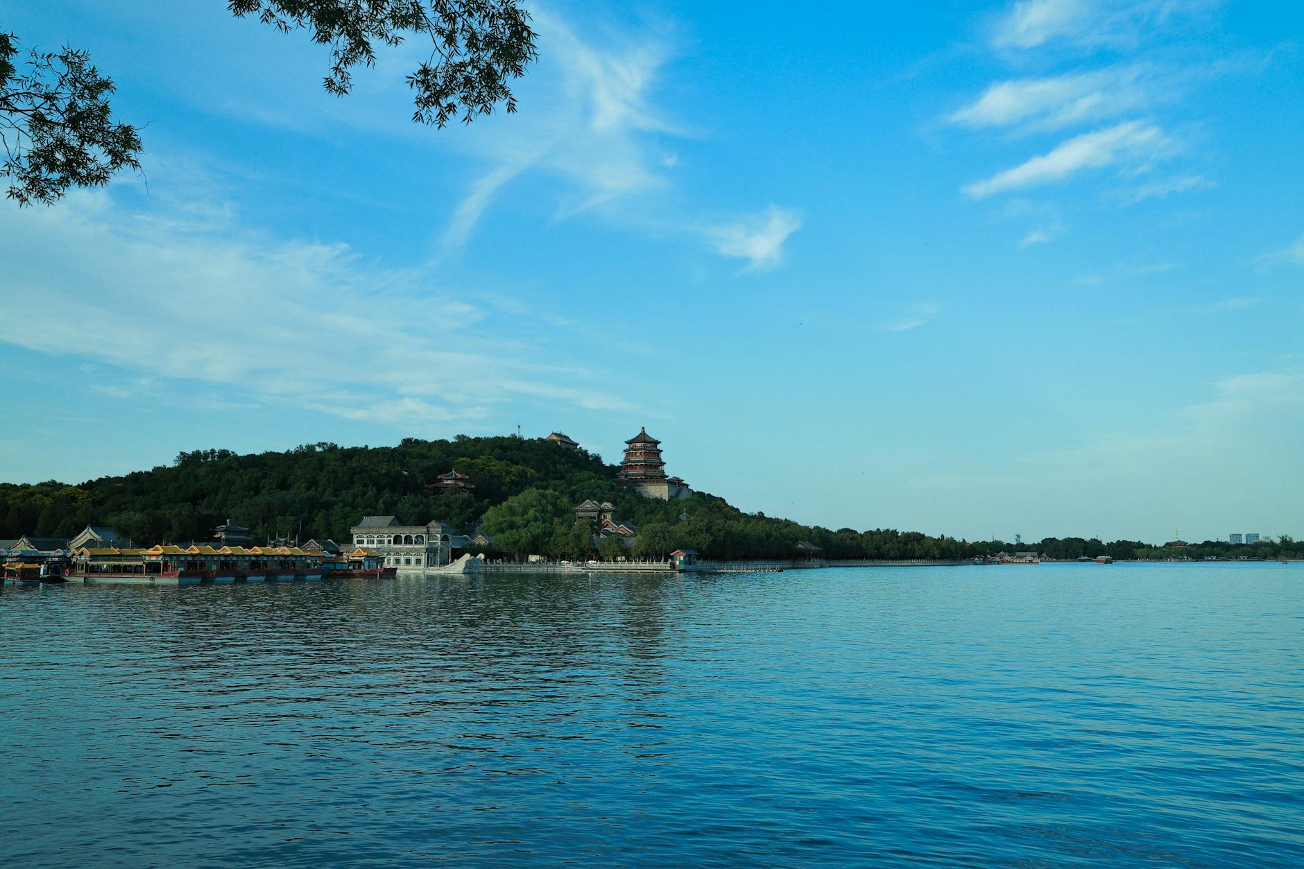 A scenic view of the Summer Palace in Beijing with lush greenery and a calm lake under a bright blue sky.