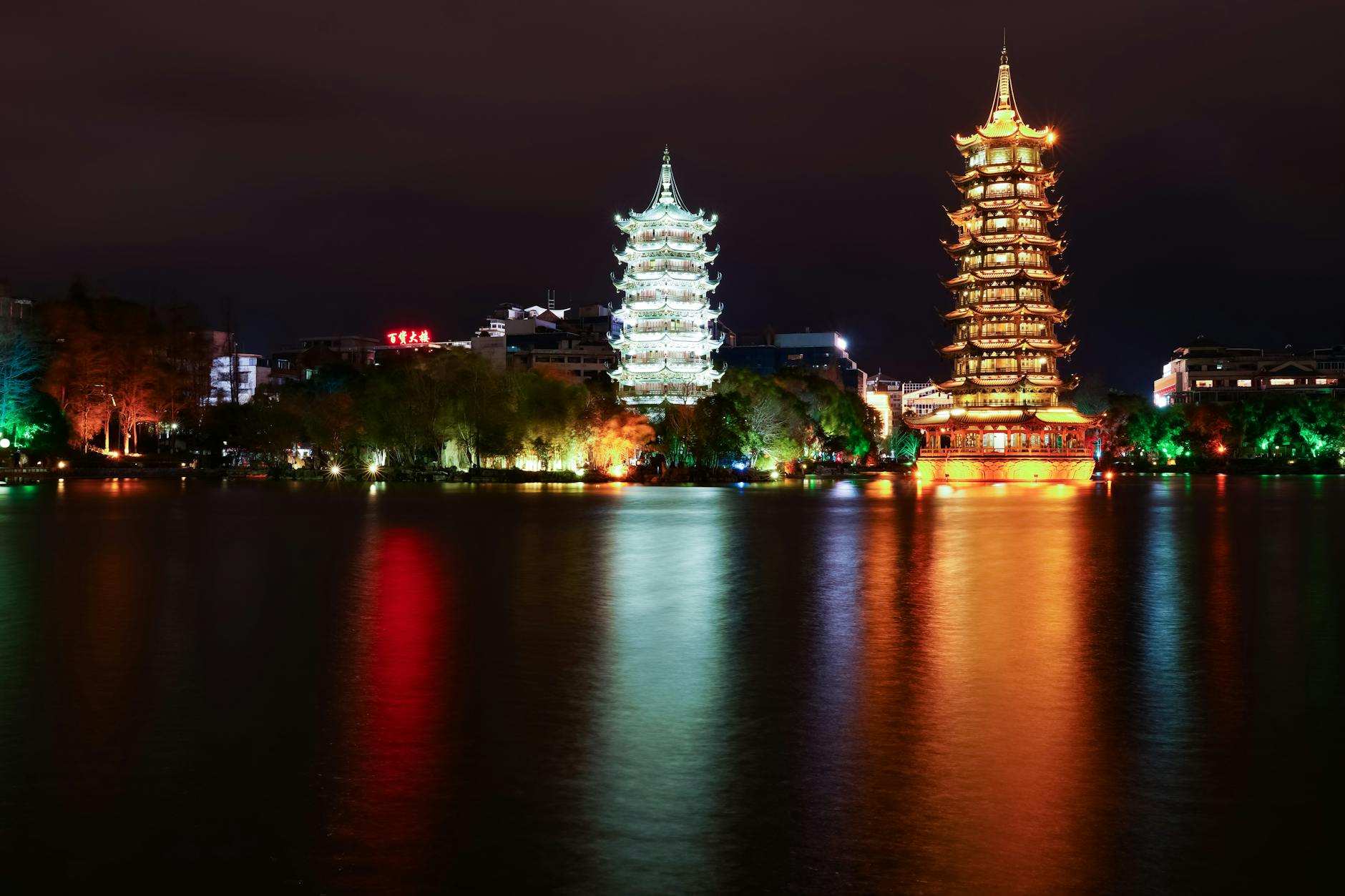 A stunning night view of the illuminated Sun and Moon Pagodas reflecting in a serene river in Guilin, China.