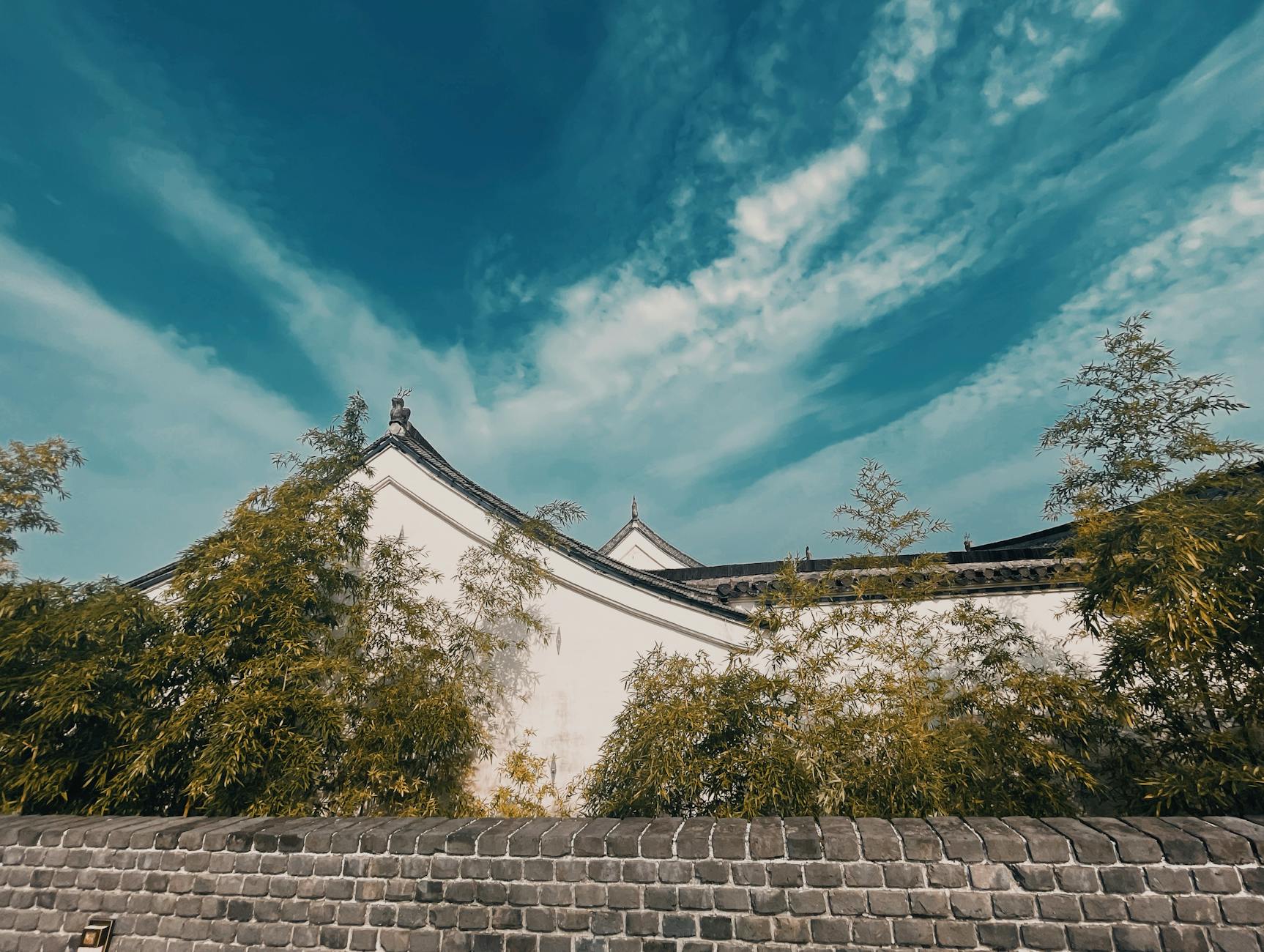 A picturesque view of traditional Chinese architecture surrounded by bamboo trees under a vibrant blue sky.