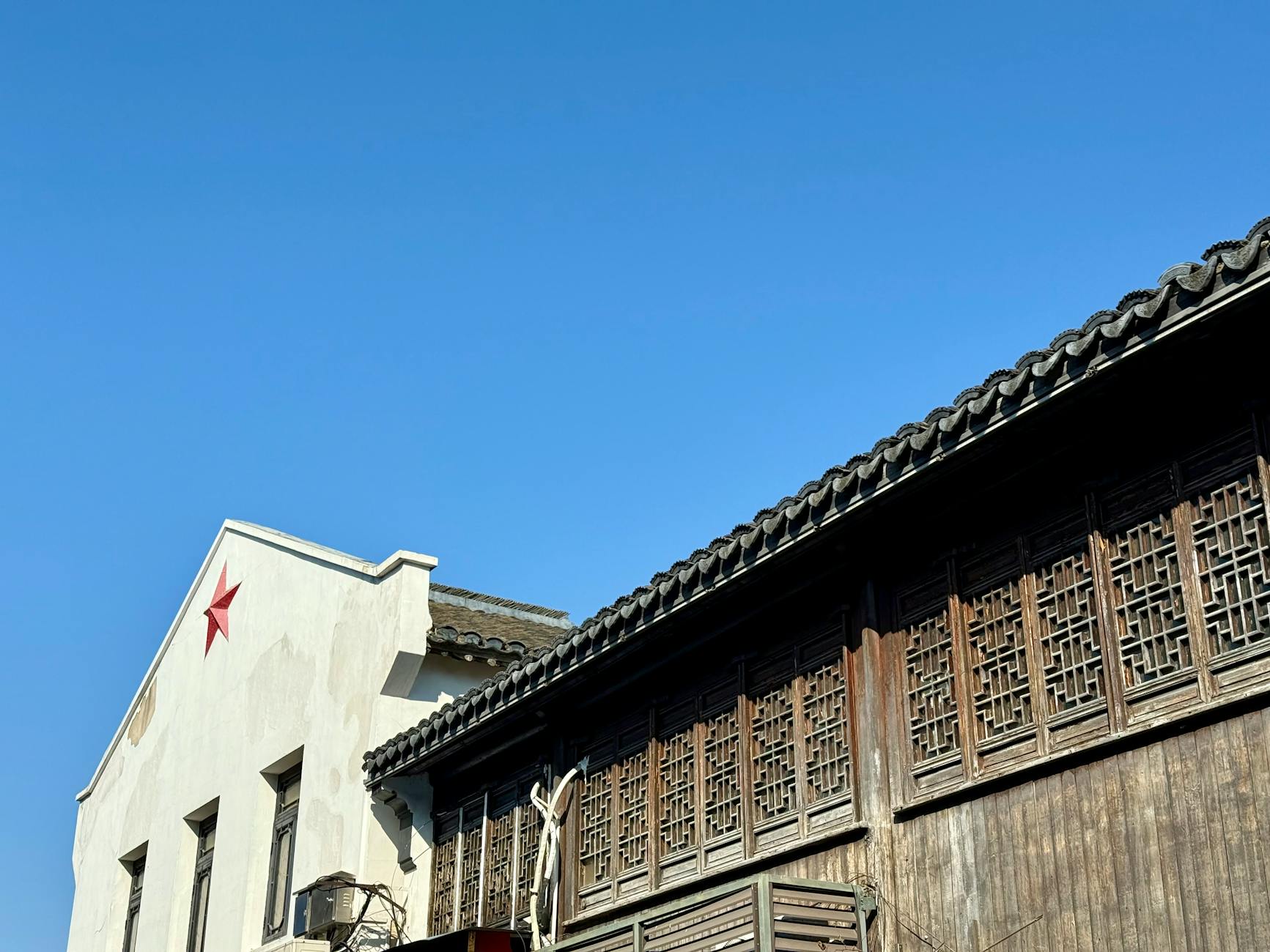 Traditional Chinese building with wooden lattice windows and red star emblem against a clear blue sky.