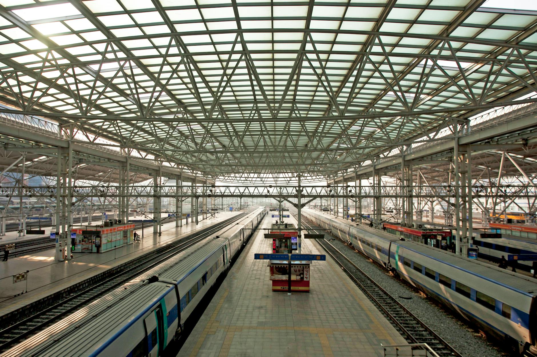 Spacious railway station with multiple platforms and trains under a steel glass roof.