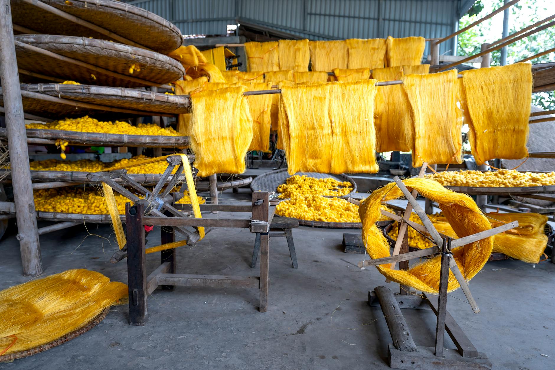 Vibrant yellow silk threads drying in a traditional artisan workshop setting.