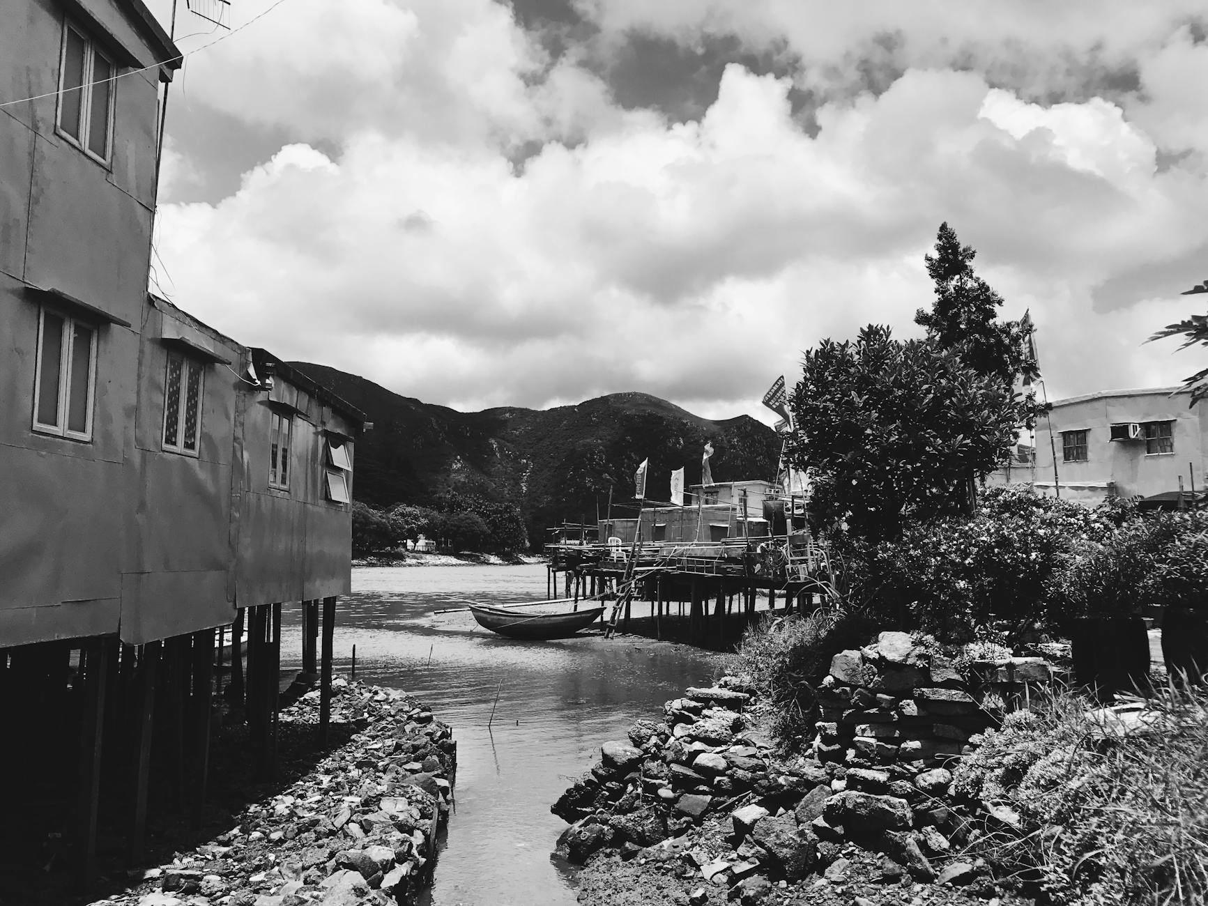 Black and white view of Tai O Fishing Village in Hong Kong's New Territories with wooden houses and mountains.