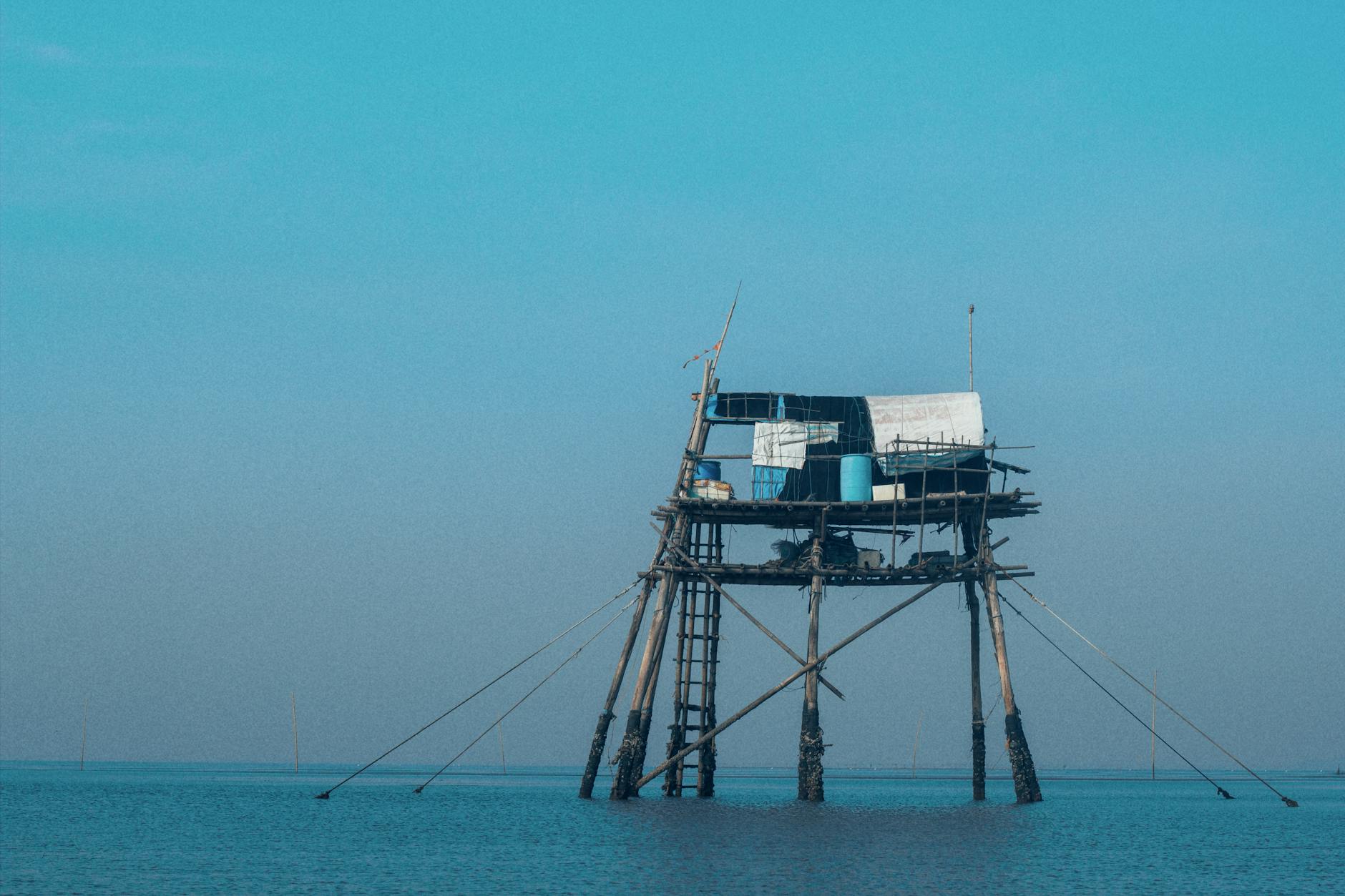 A rustic fishing hut set on stilts over calm blue water in Thai Binh, Vietnam.